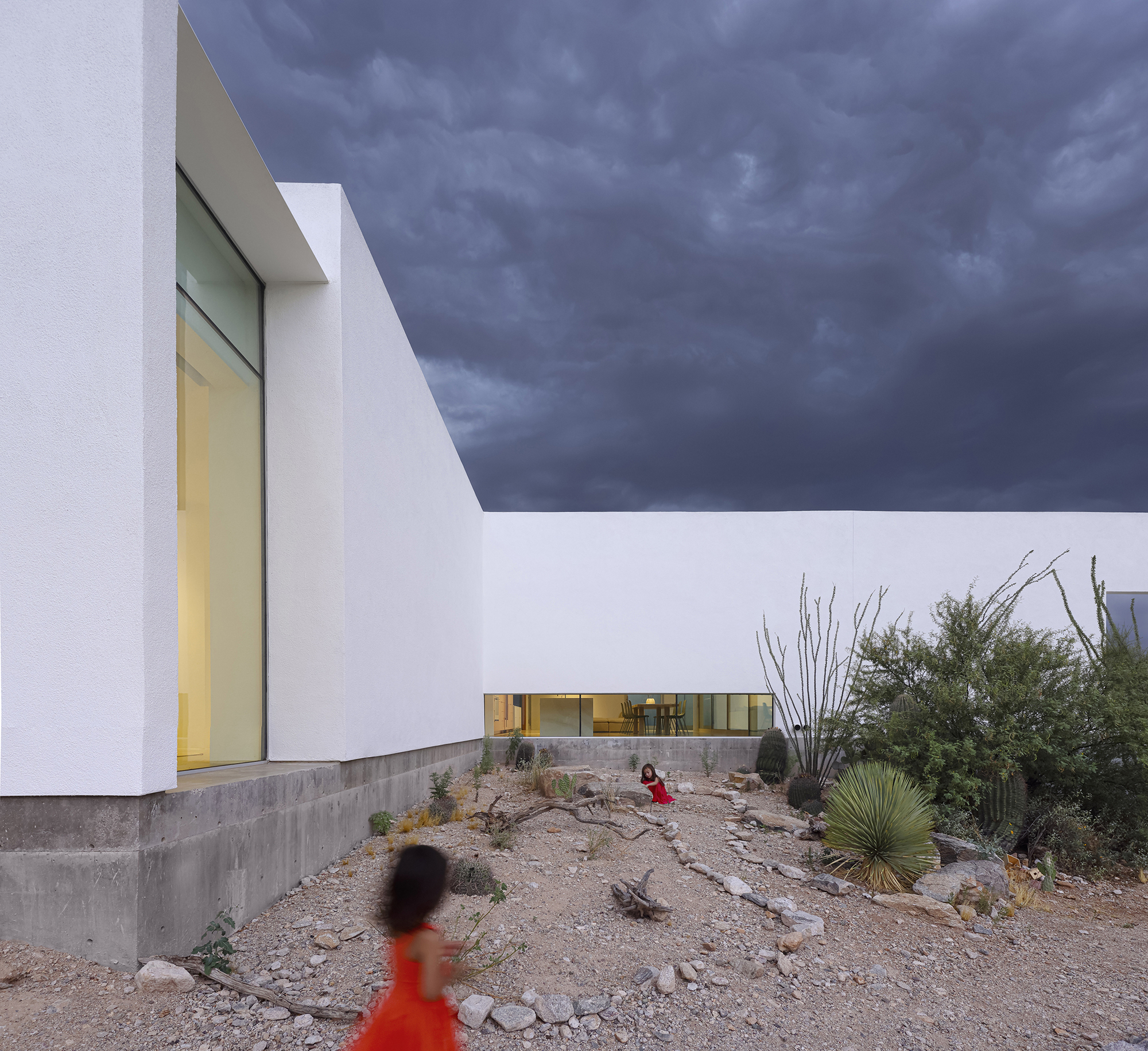 Courtyard with native desert plantings, ocotillo, and children walking beneath dramatic storm sky