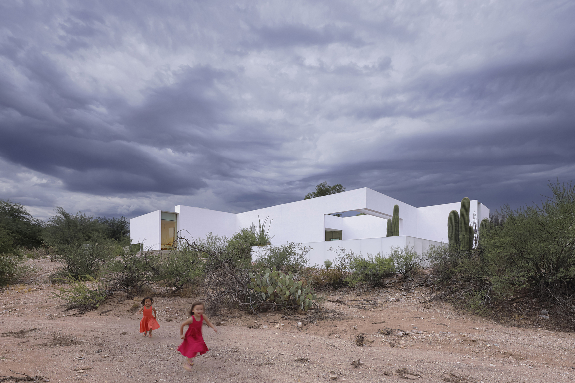 White geometric volumes with flat roofs and cutouts amid desert scrub with two children playing