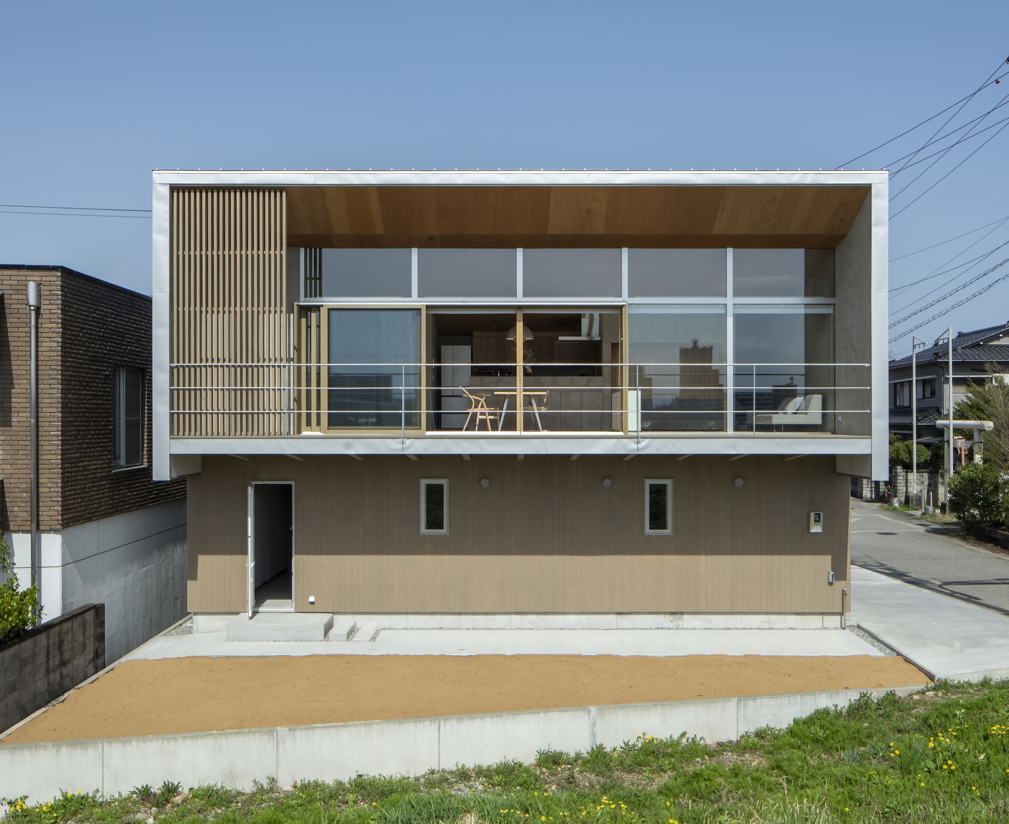 Street view showing the two-story facade with vertical timber slats, glazed upper level terrace, and beige concrete base
