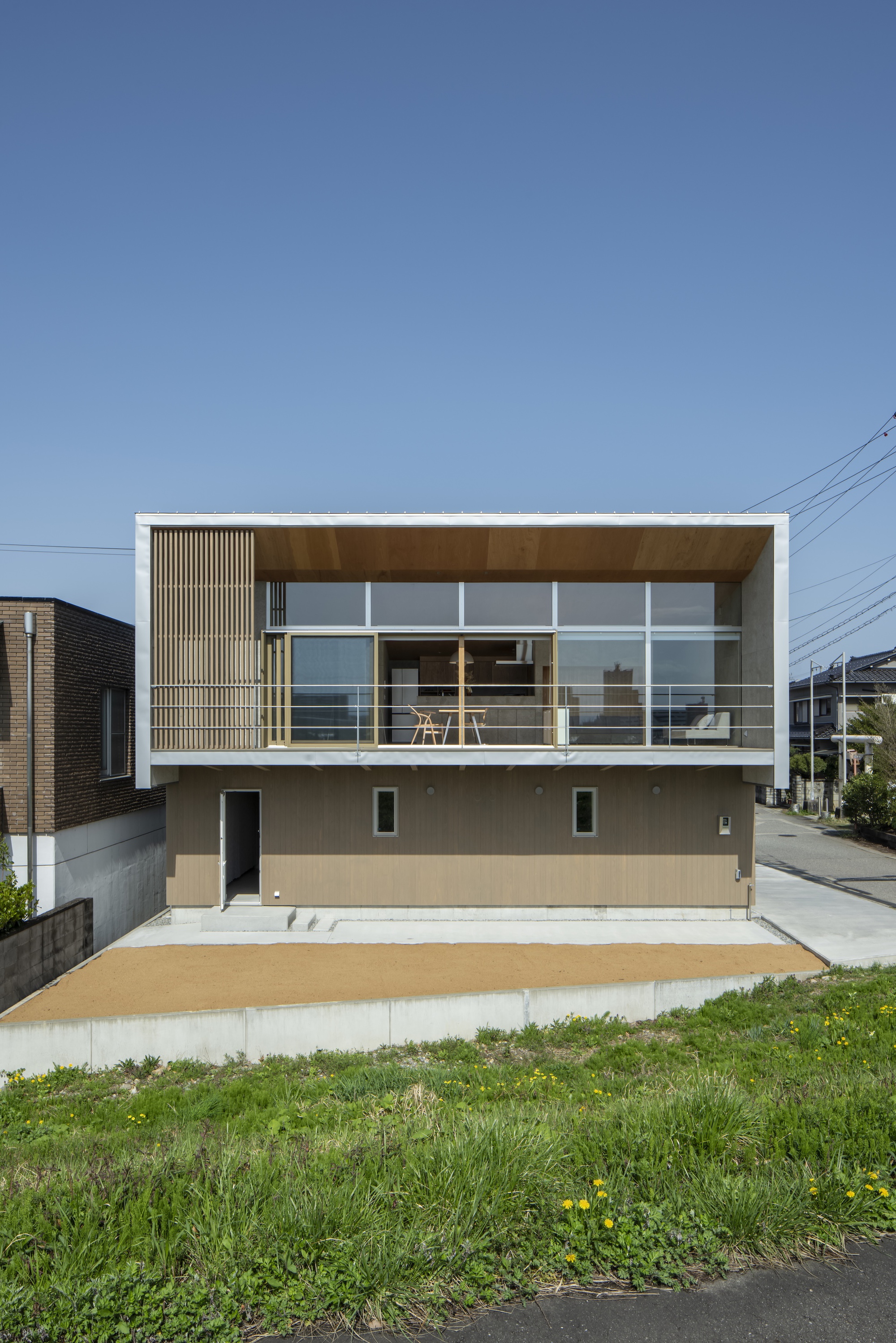 Front elevation with upper level timber screening, glass balustrade, and grassy foreground under clear sky