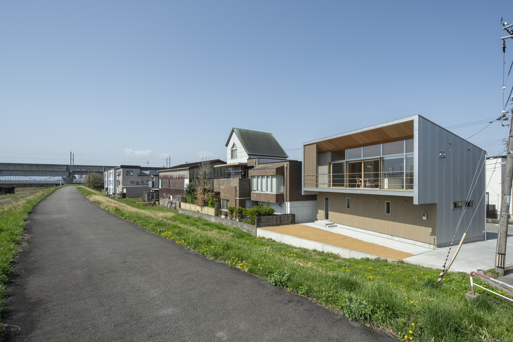 Diagonal view from adjacent path showing the house amid neighboring buildings and grassy embankment