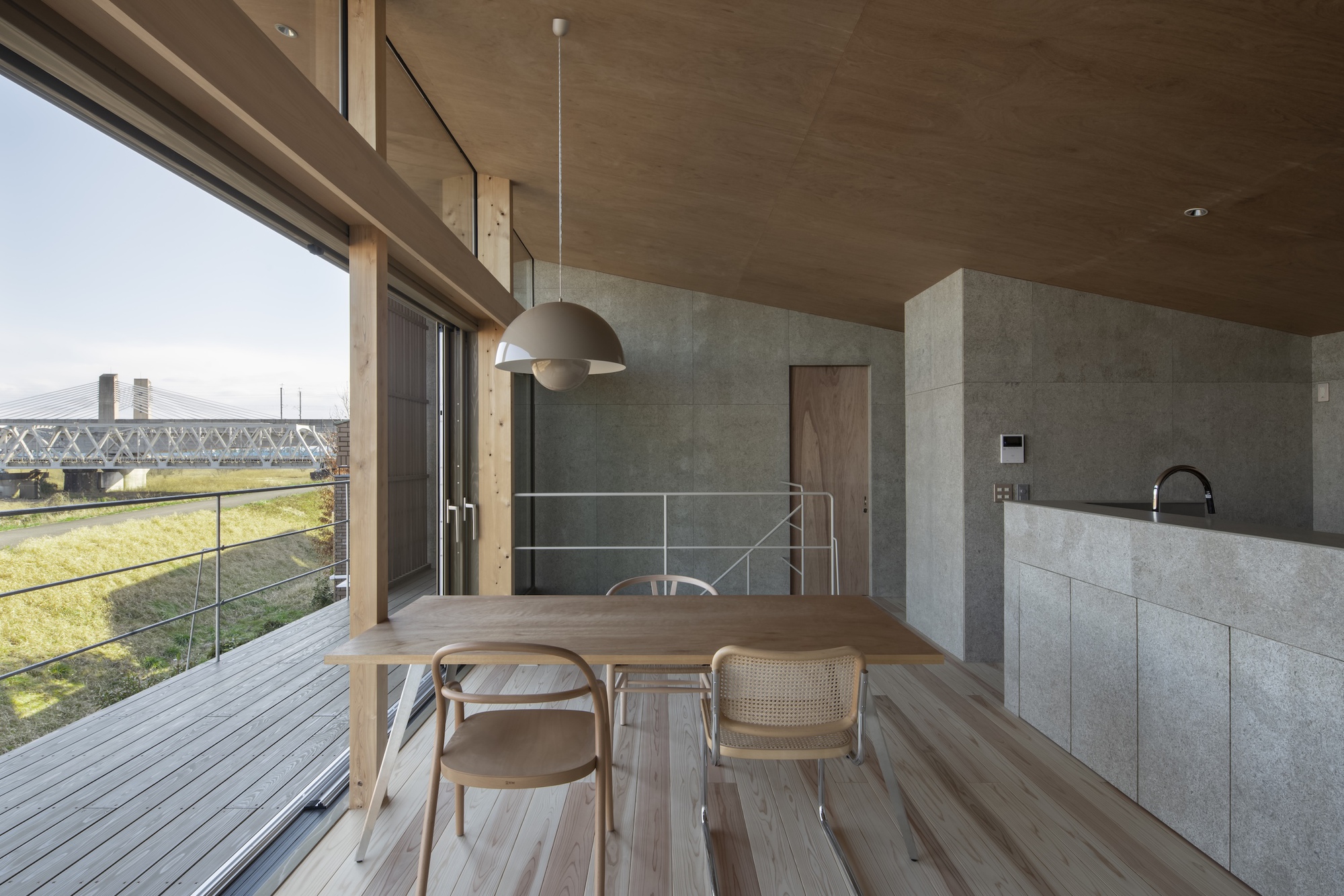 Dining area with timber table, pendant light, and concrete kitchen island overlooking the terrace