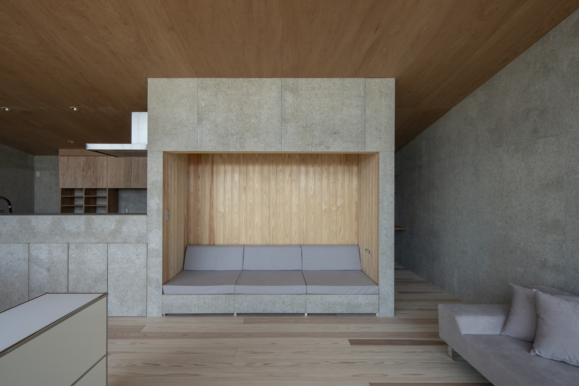 Interior living space with built-in timber bench niche framed by concrete walls under a wood ceiling