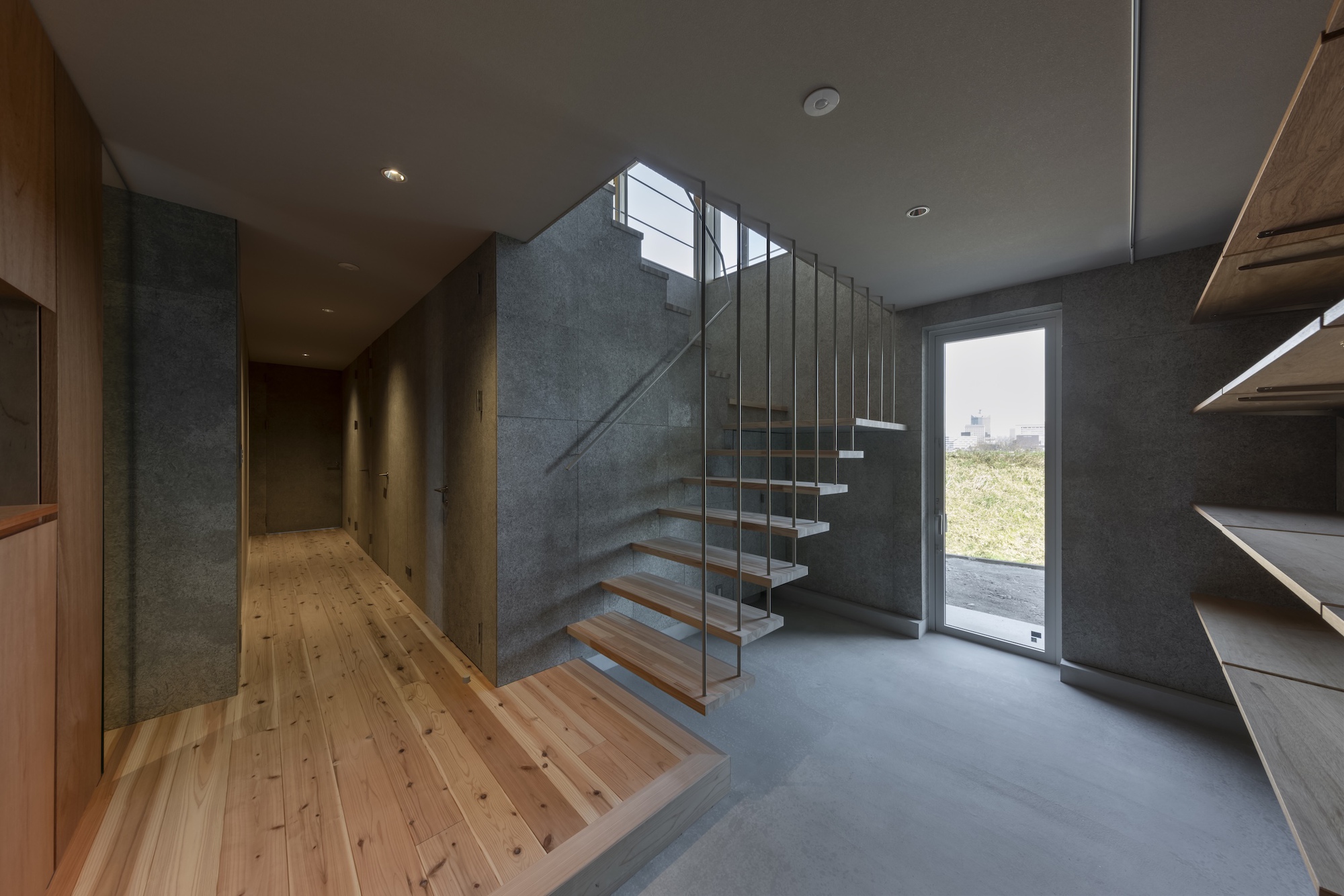Entry hall with floating timber staircase, glass railings, and grey concrete walls beside timber flooring