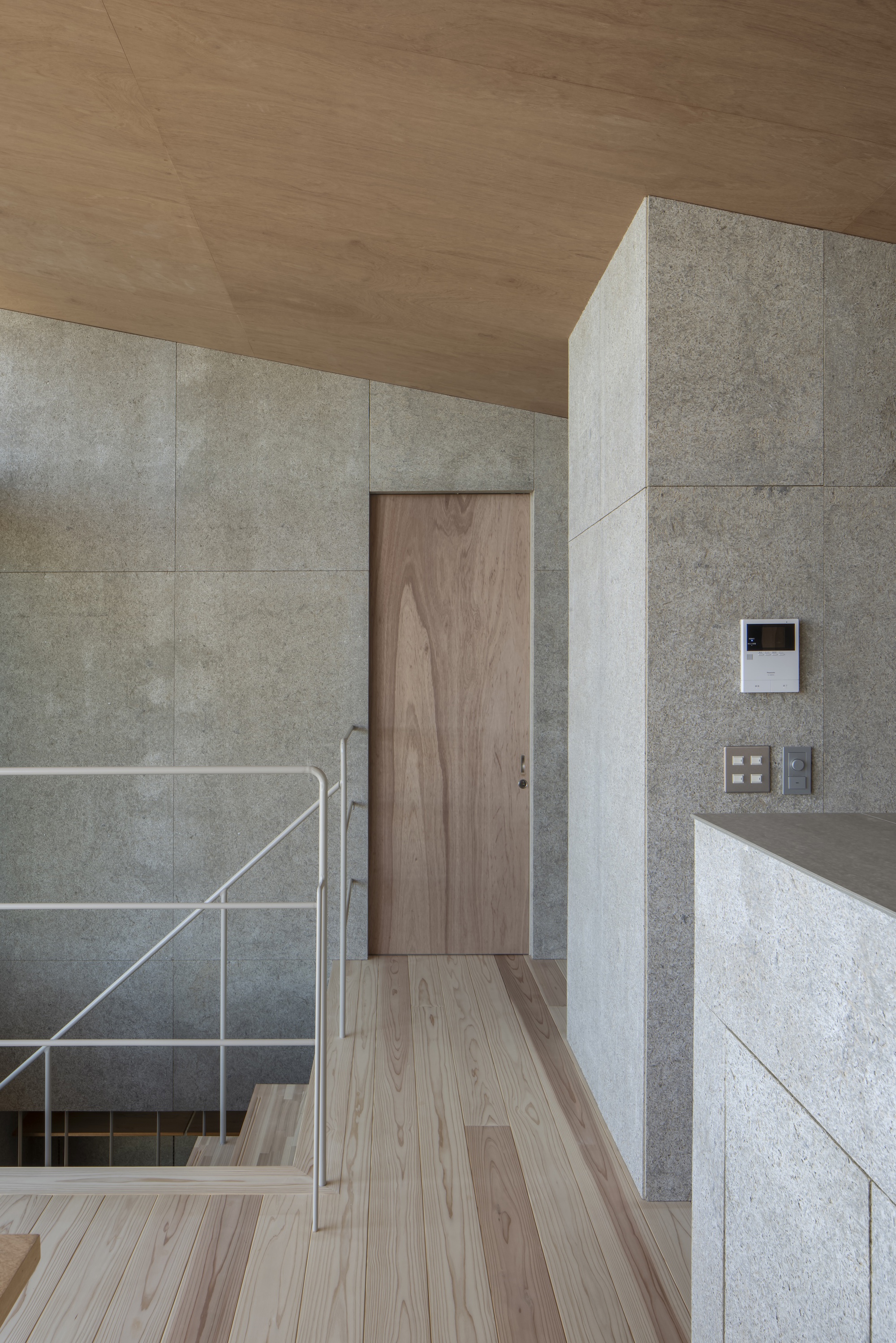 Upper level landing with concrete panel walls, timber door and ceiling, and steel stair railing