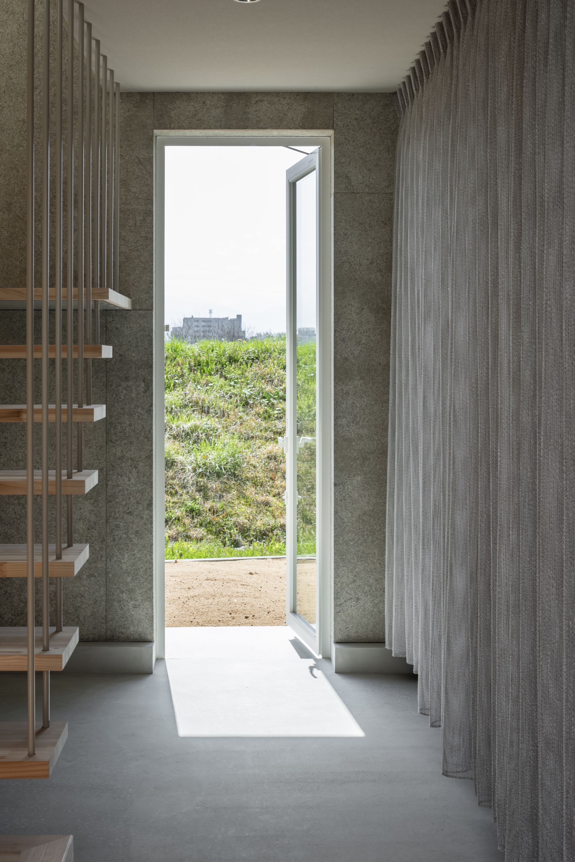 Open doorway in concrete wall with vertical screen panels flooding light across polished floor