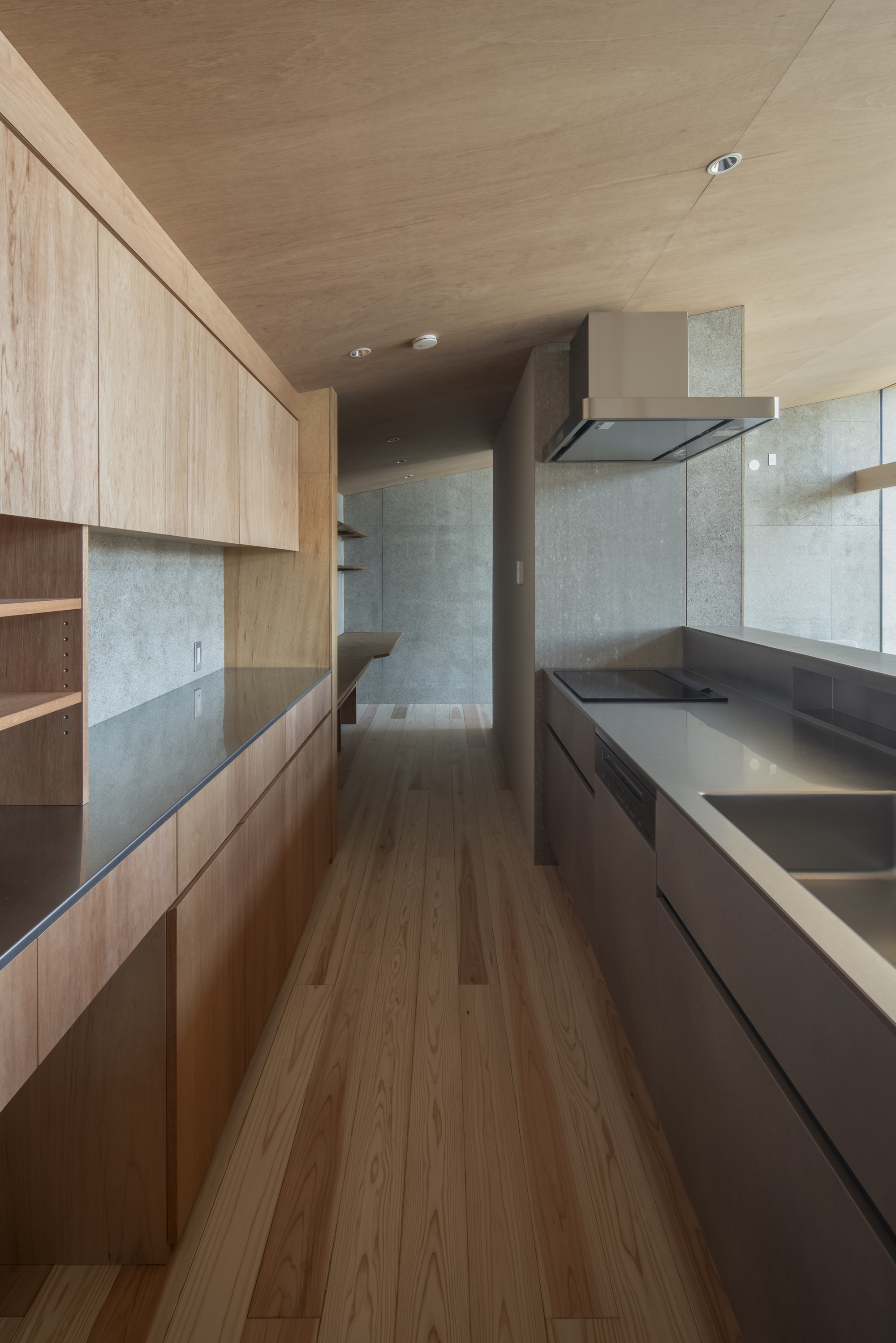 Galley kitchen with timber cabinetry, dark countertop, and concrete panel backsplash under plywood ceiling