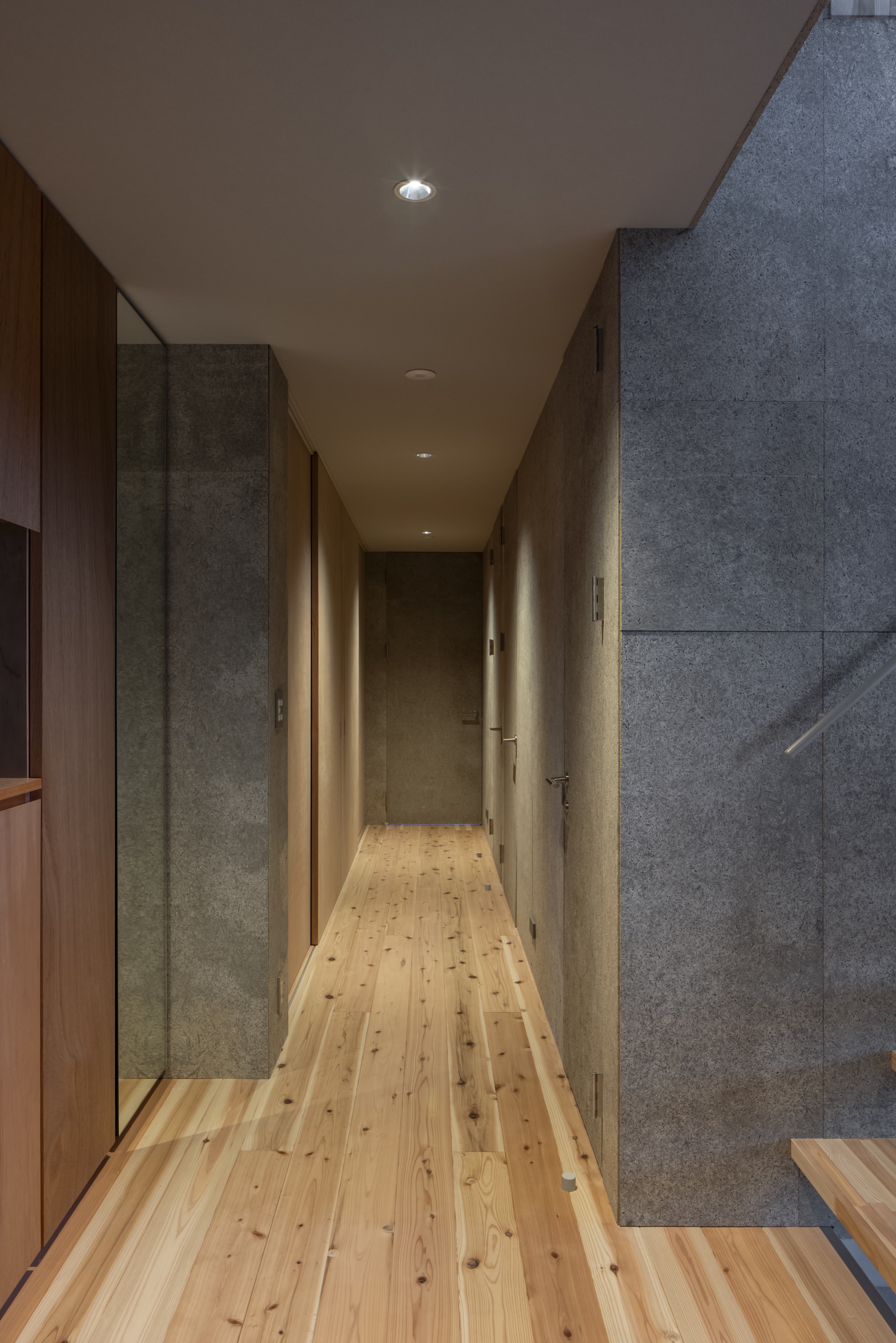 Narrow hallway with concrete walls, timber flooring, and recessed lighting along plywood ceiling