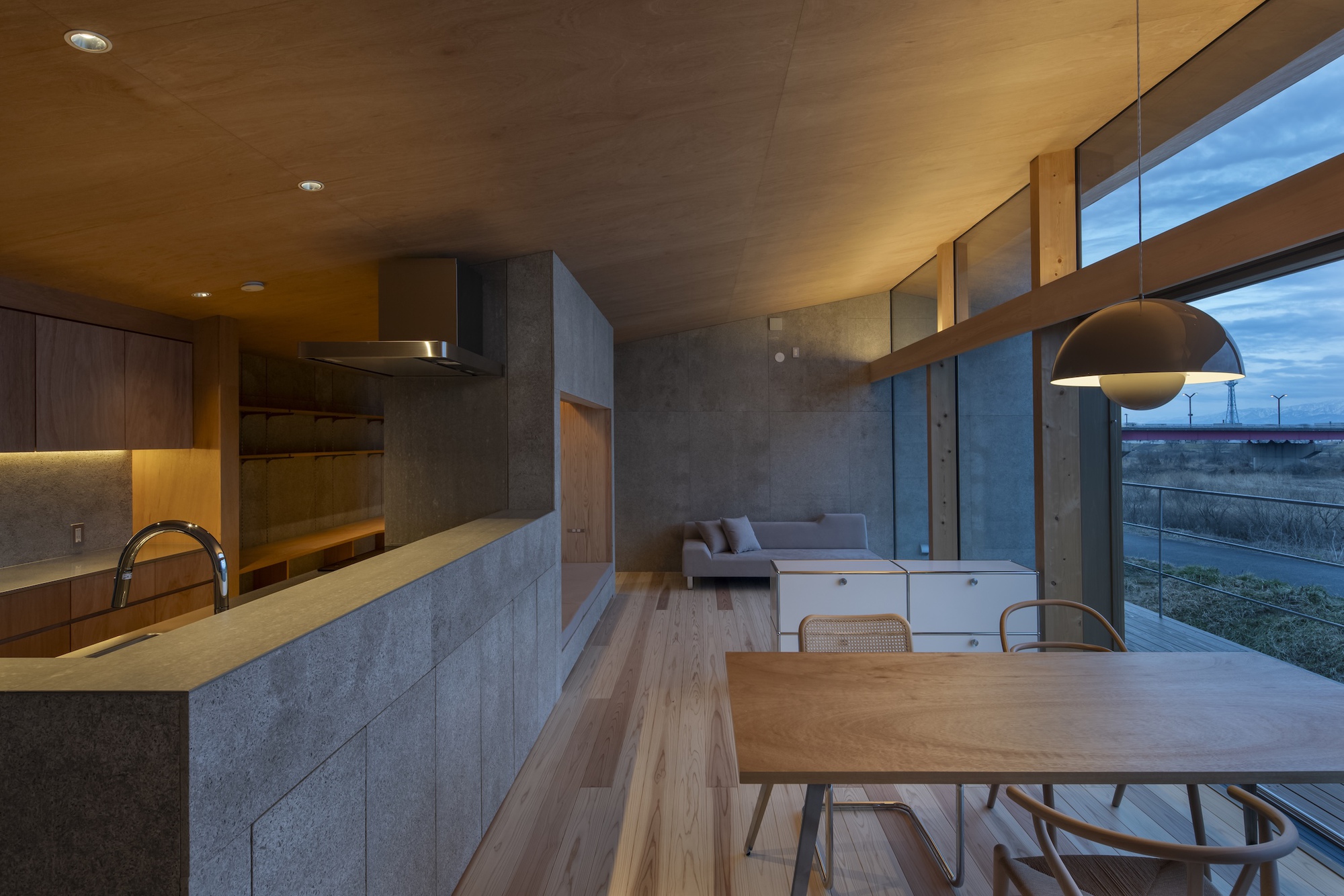Open-plan living space with concrete kitchen island, timber dining table and clerestory windows at dusk