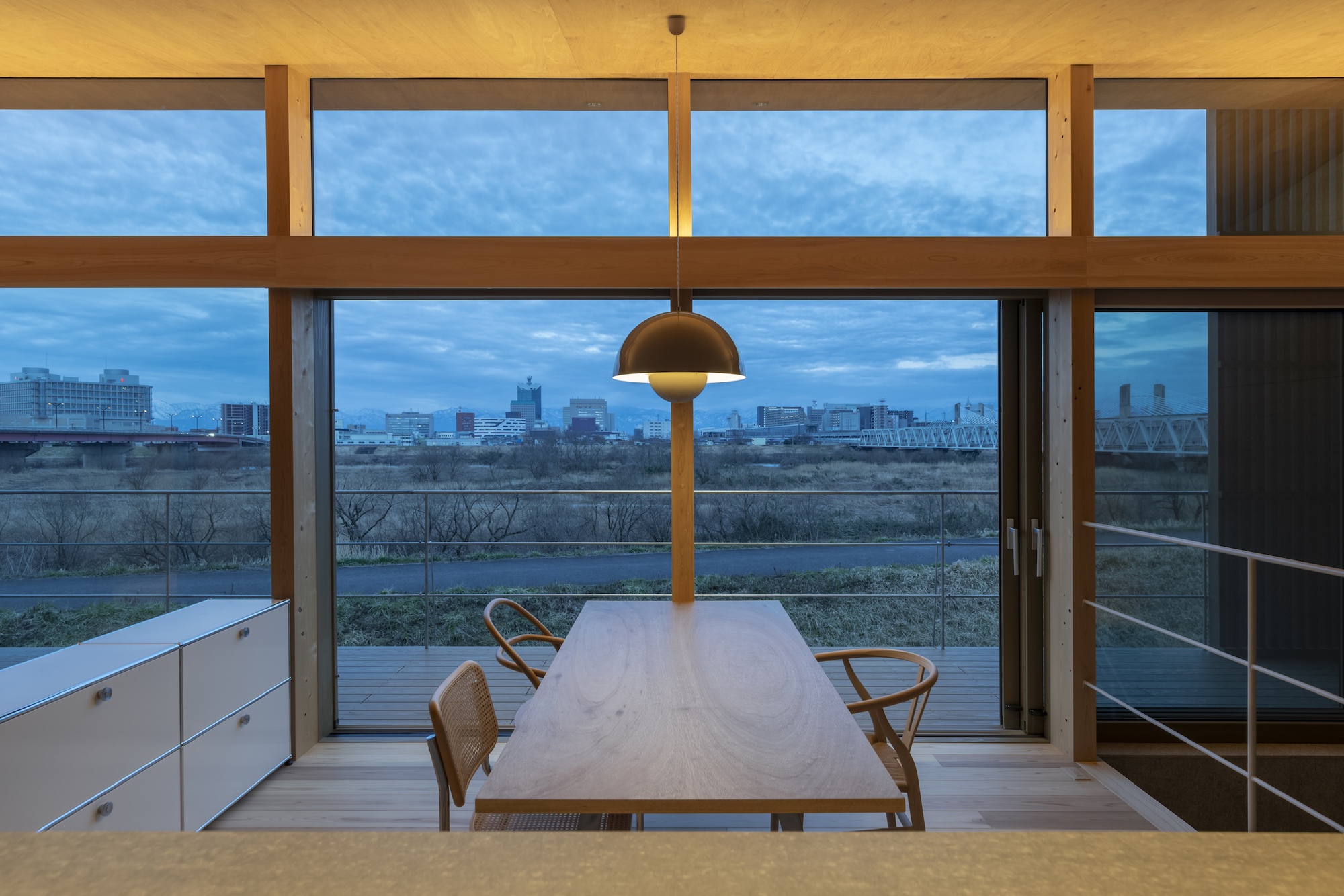 Dining table framed by horizontal timber windows with a view of the river at twilight