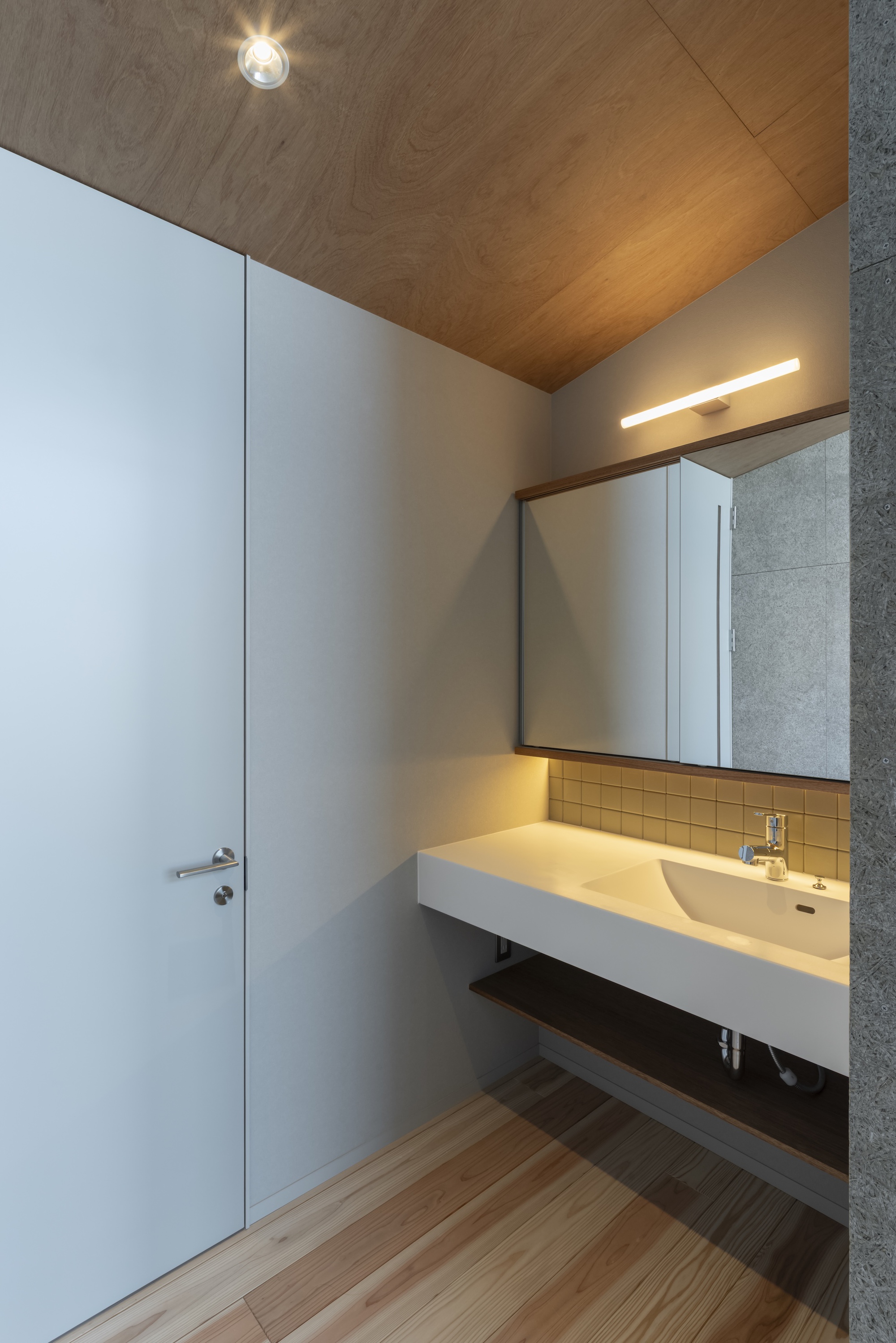 Bathroom vanity with cantilevered counter, backlit mirror and angled timber ceiling