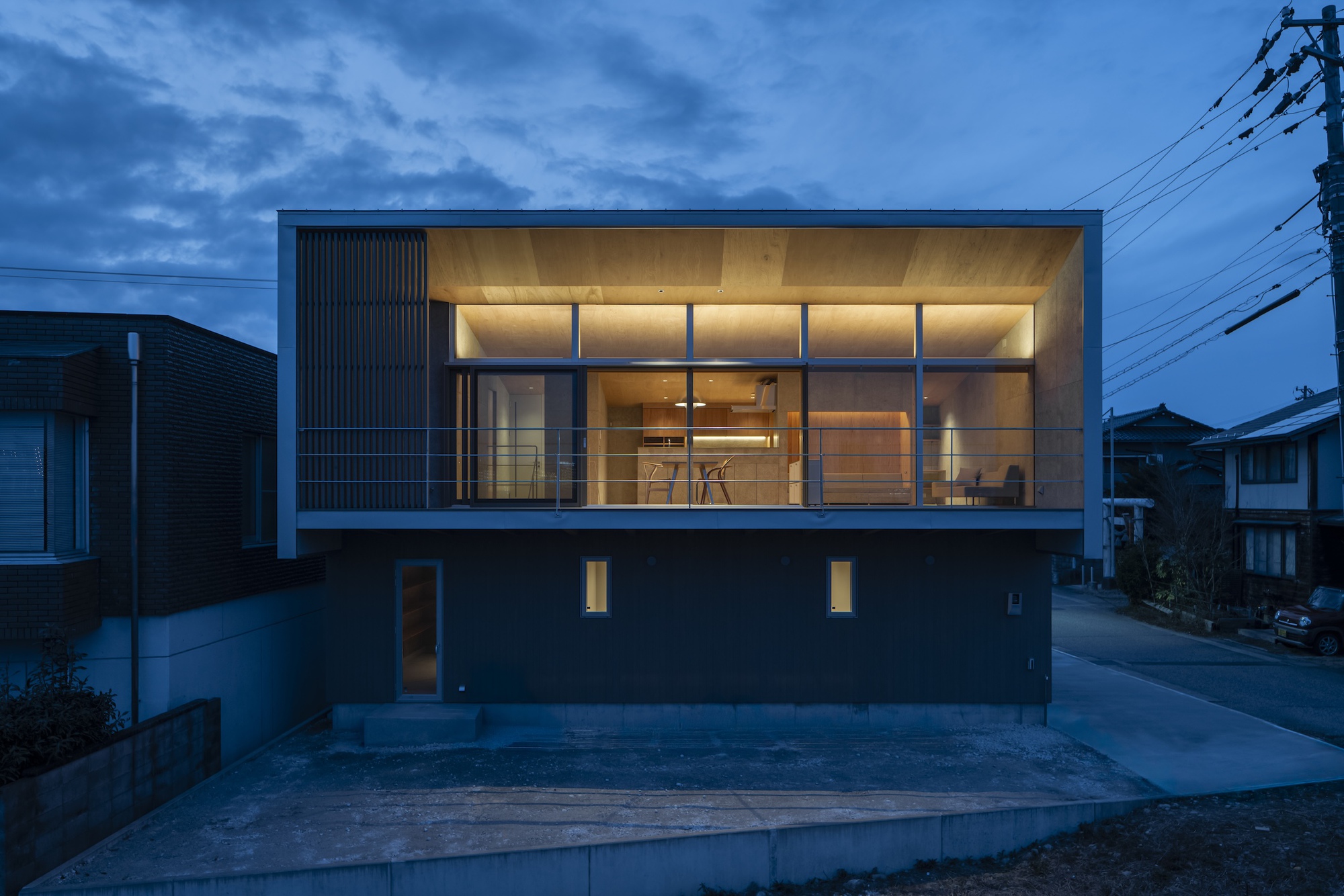 Street facade with ribbed metal cladding and glazed upper volume illuminated at dusk