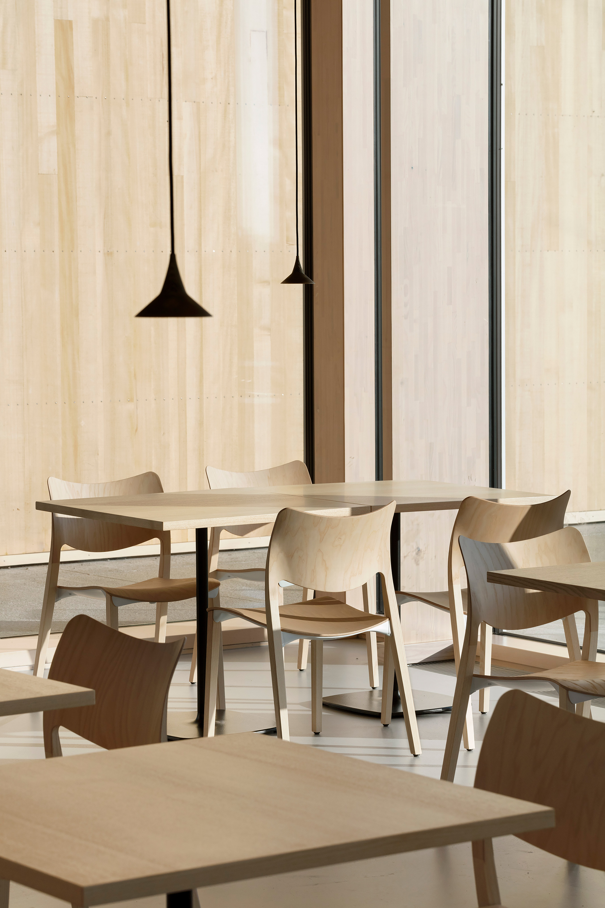 Dining tables with pendant lights hanging against a pale wood wall with dark vertical reveals