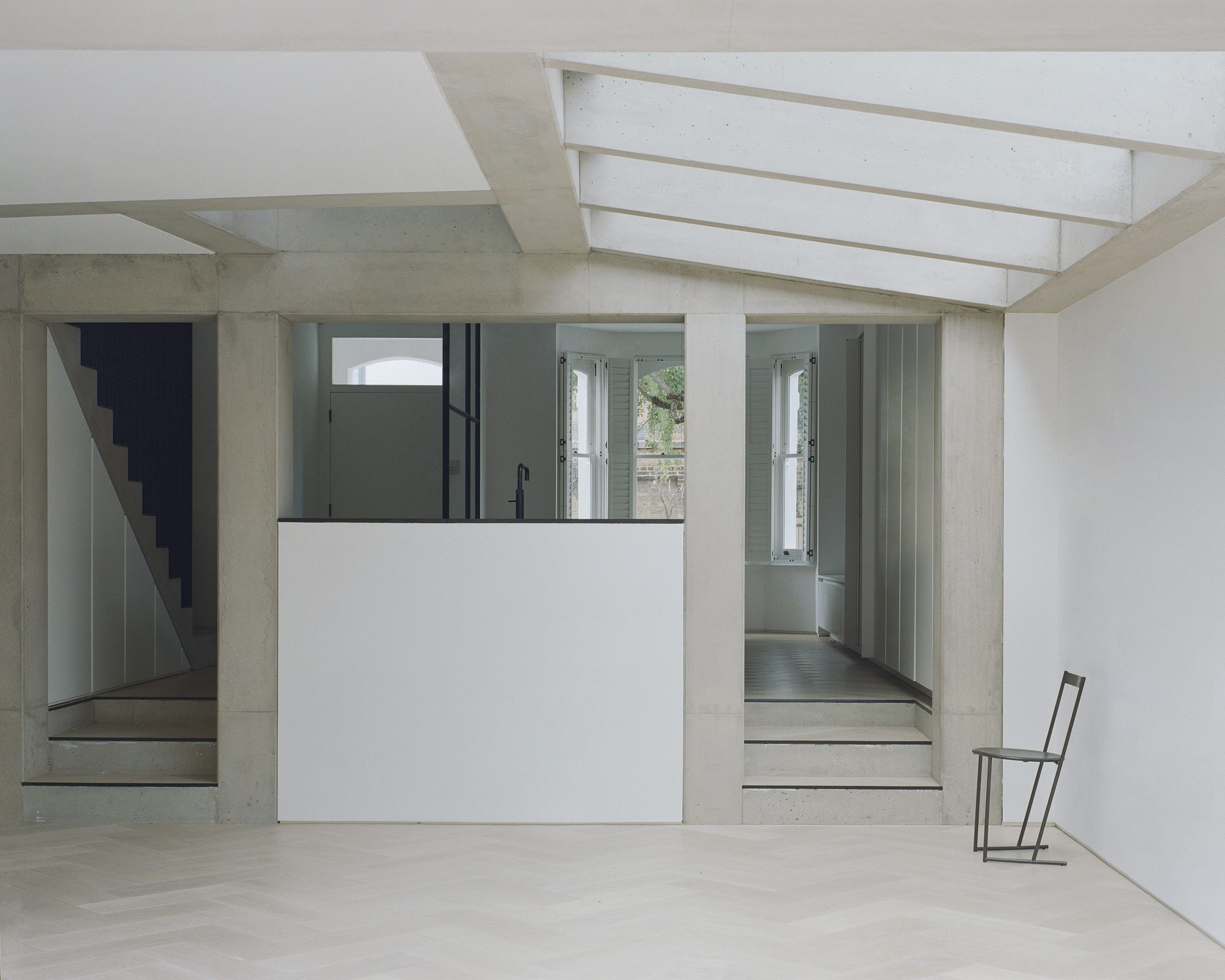 Interior room with concrete staircase and white kitchen volume beneath linear skylights