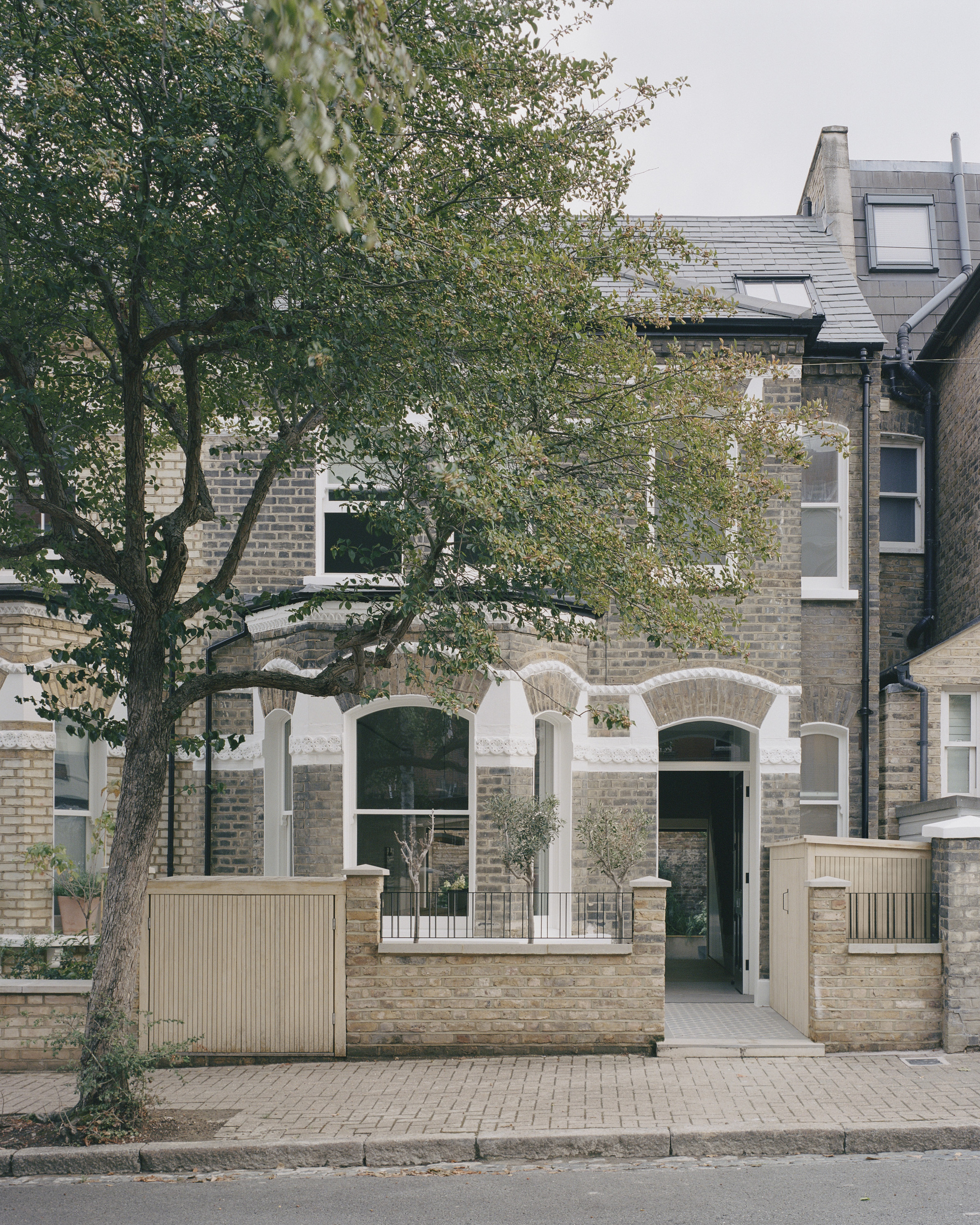 Street facade with white stucco and arched windows framed by mature tree