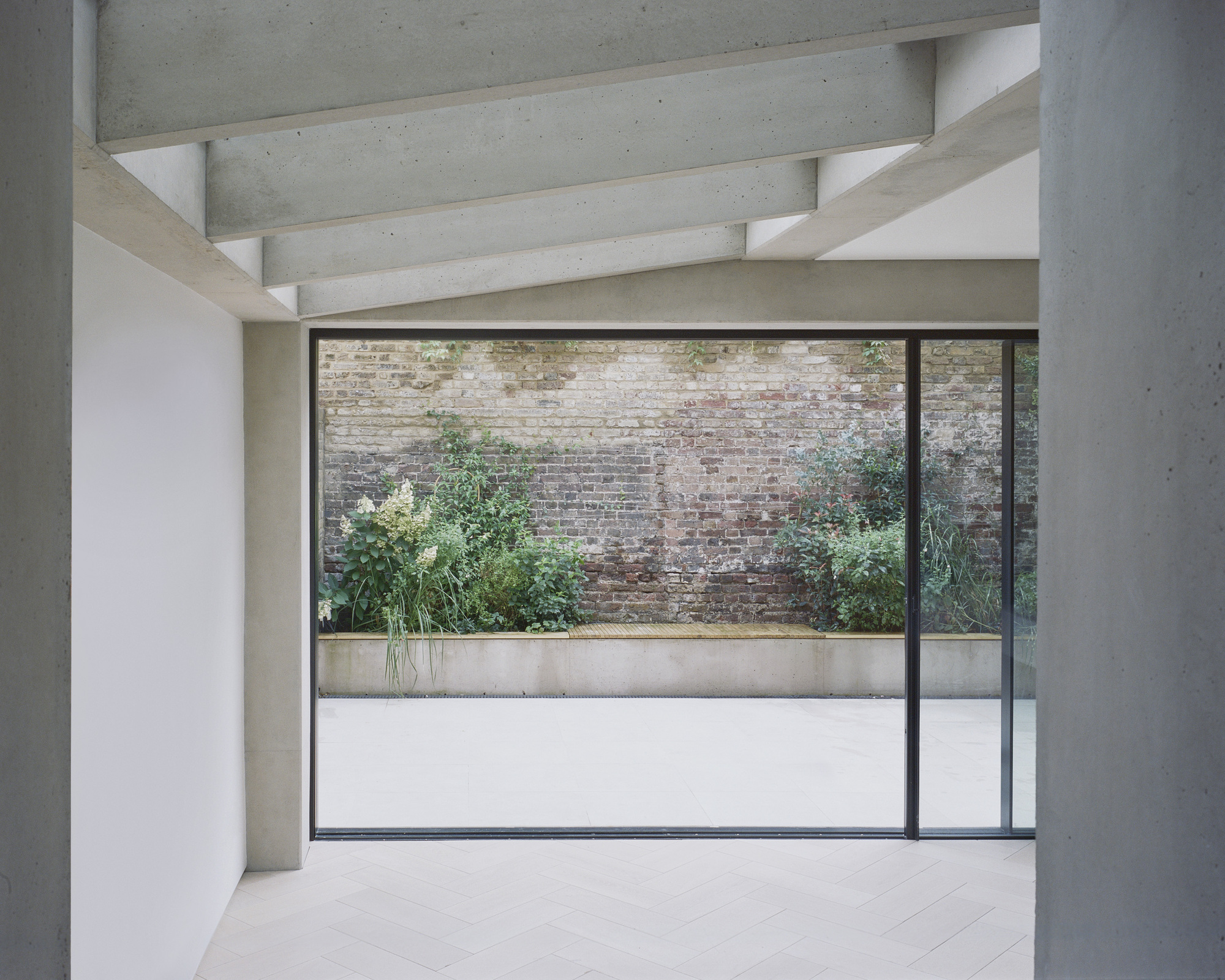 Full-height window framing courtyard with weathered brick wall and planted bed