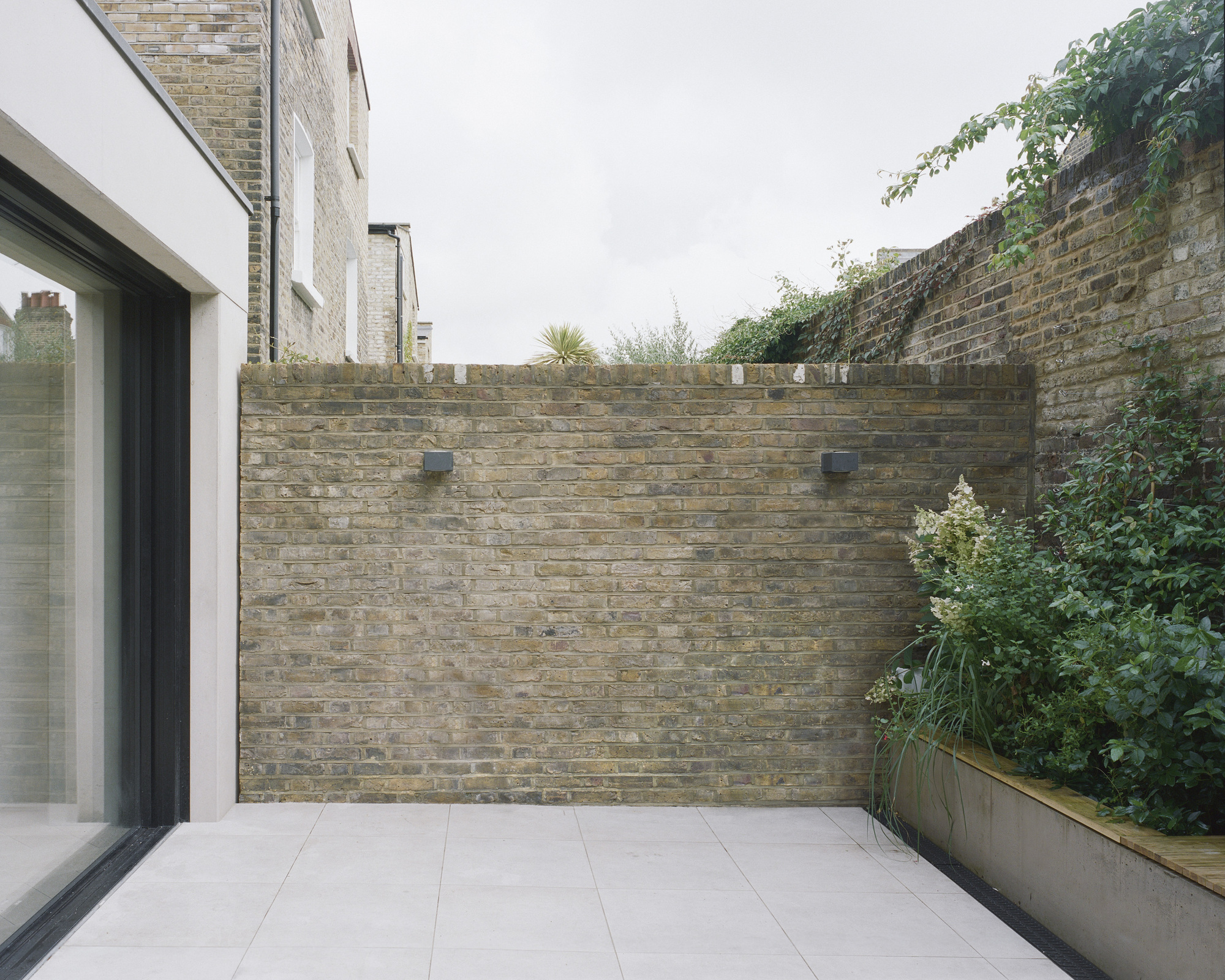 Rear courtyard terrace with buff brick walls and planted bed with greenery