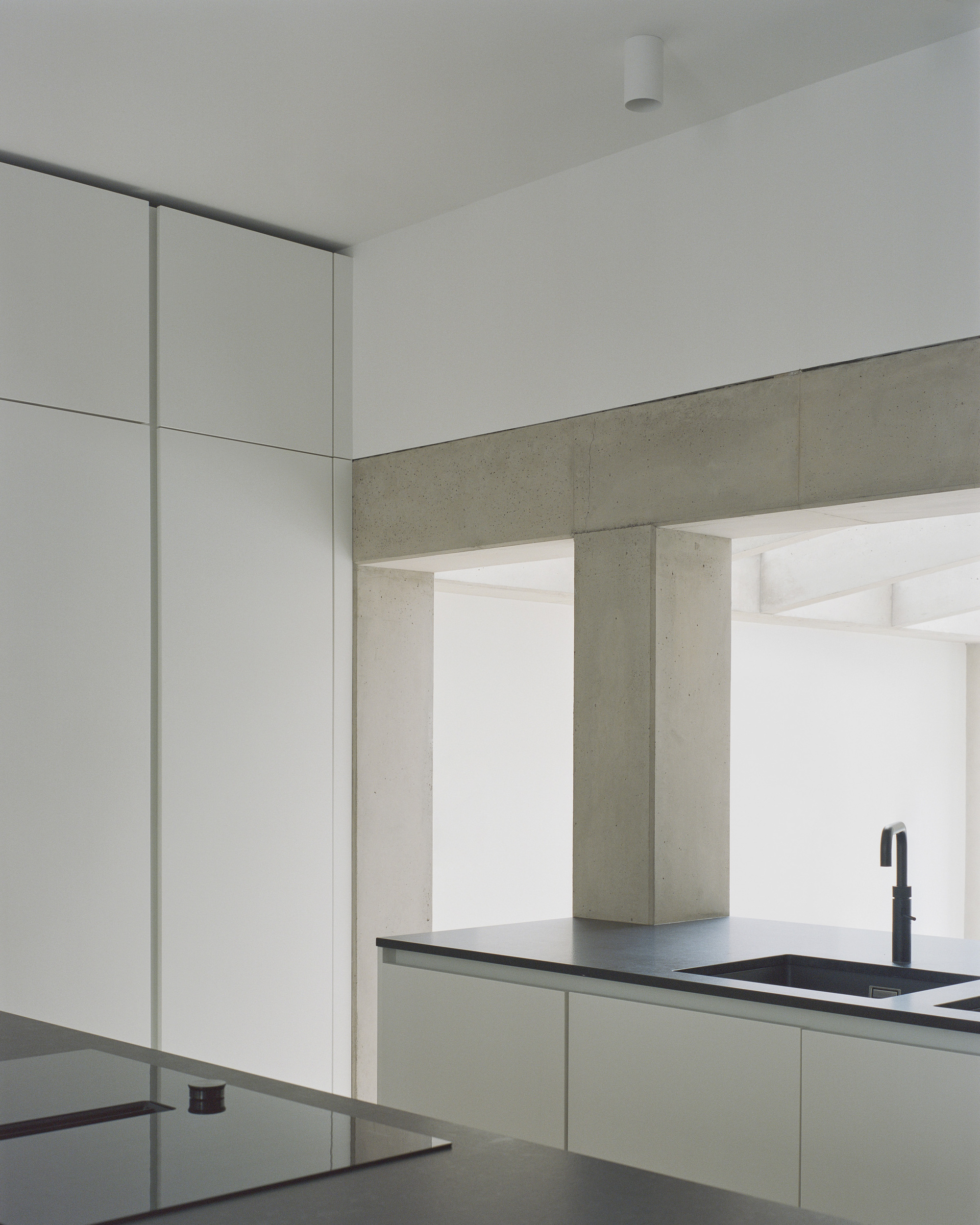 Kitchen corner showing concrete beam spanning across white cabinetry with dark countertop