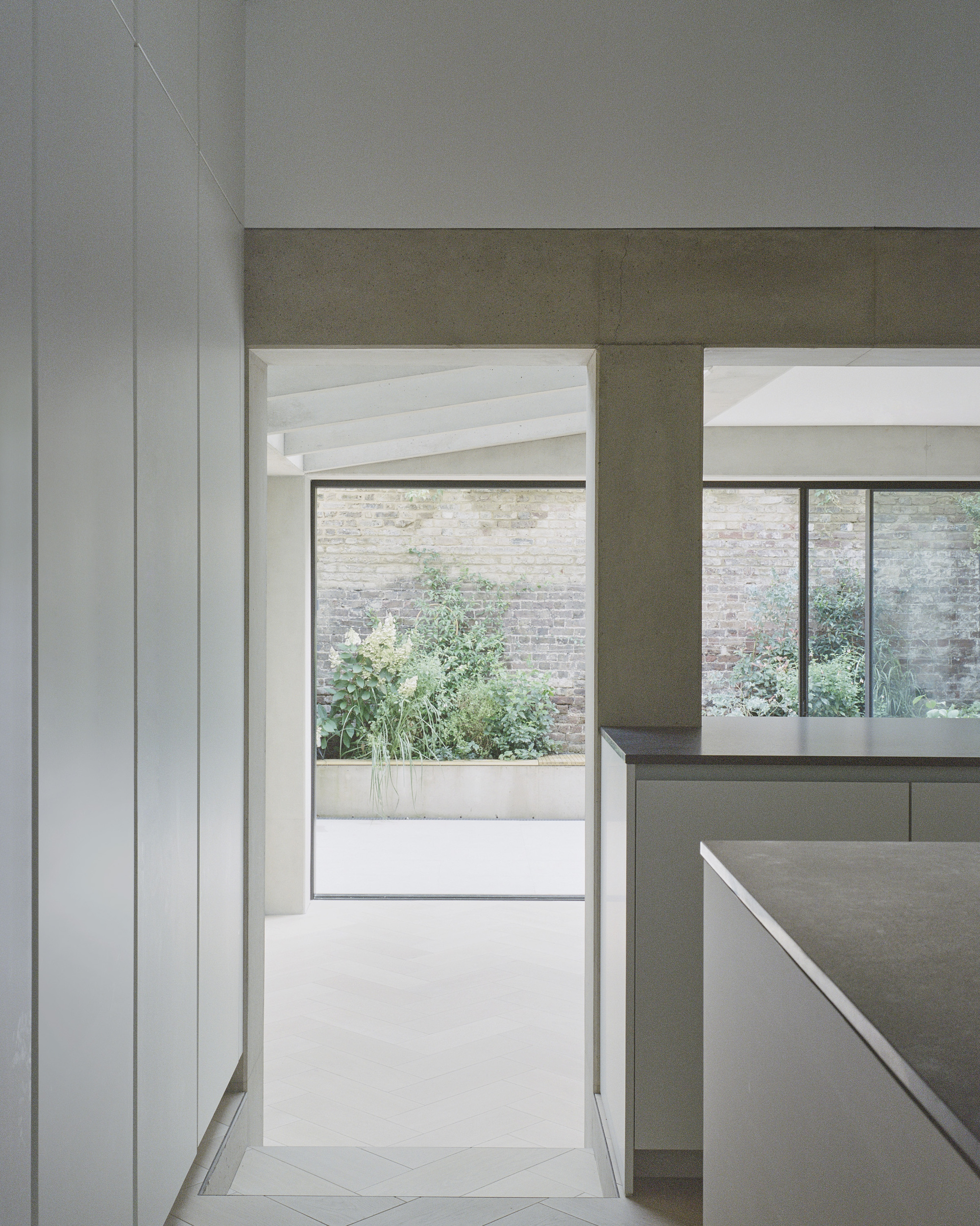 View through kitchen toward courtyard with planted greenery beyond glass doors