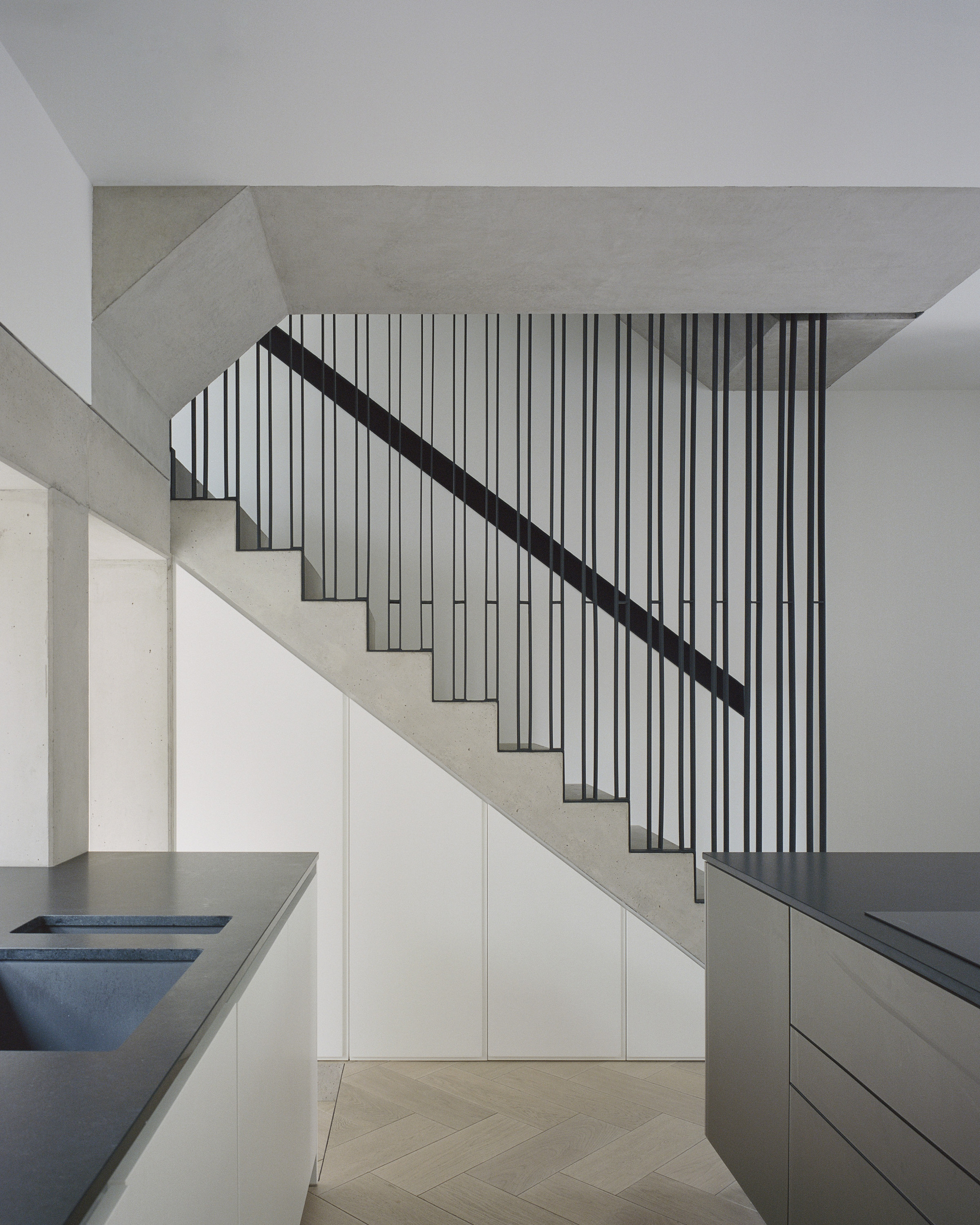 Concrete stair with vertical metal rod balustrade and dark handrail beneath sloped ceiling