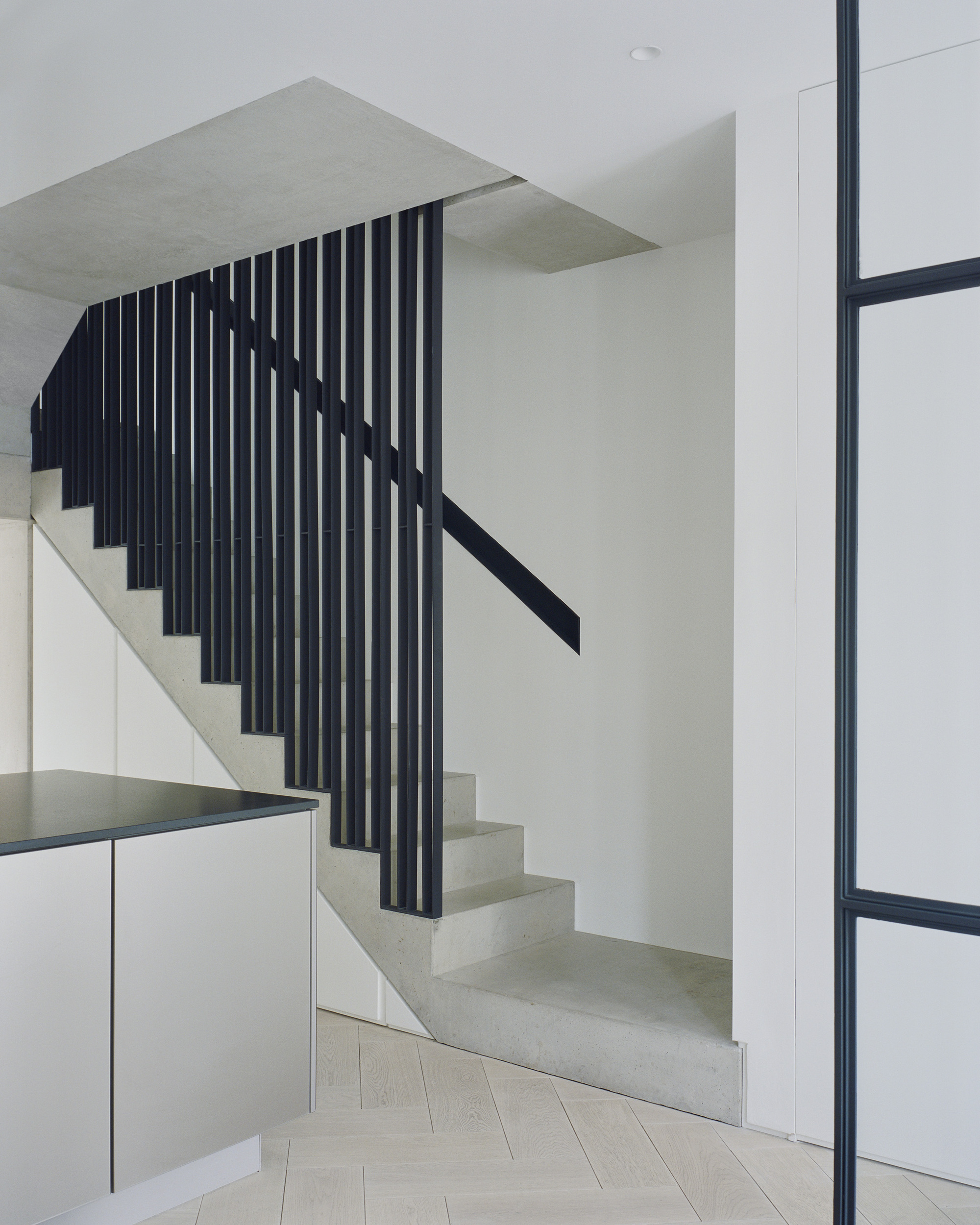 Concrete staircase with vertical black metal slat balustrade and metal handrail beside white cabinetry