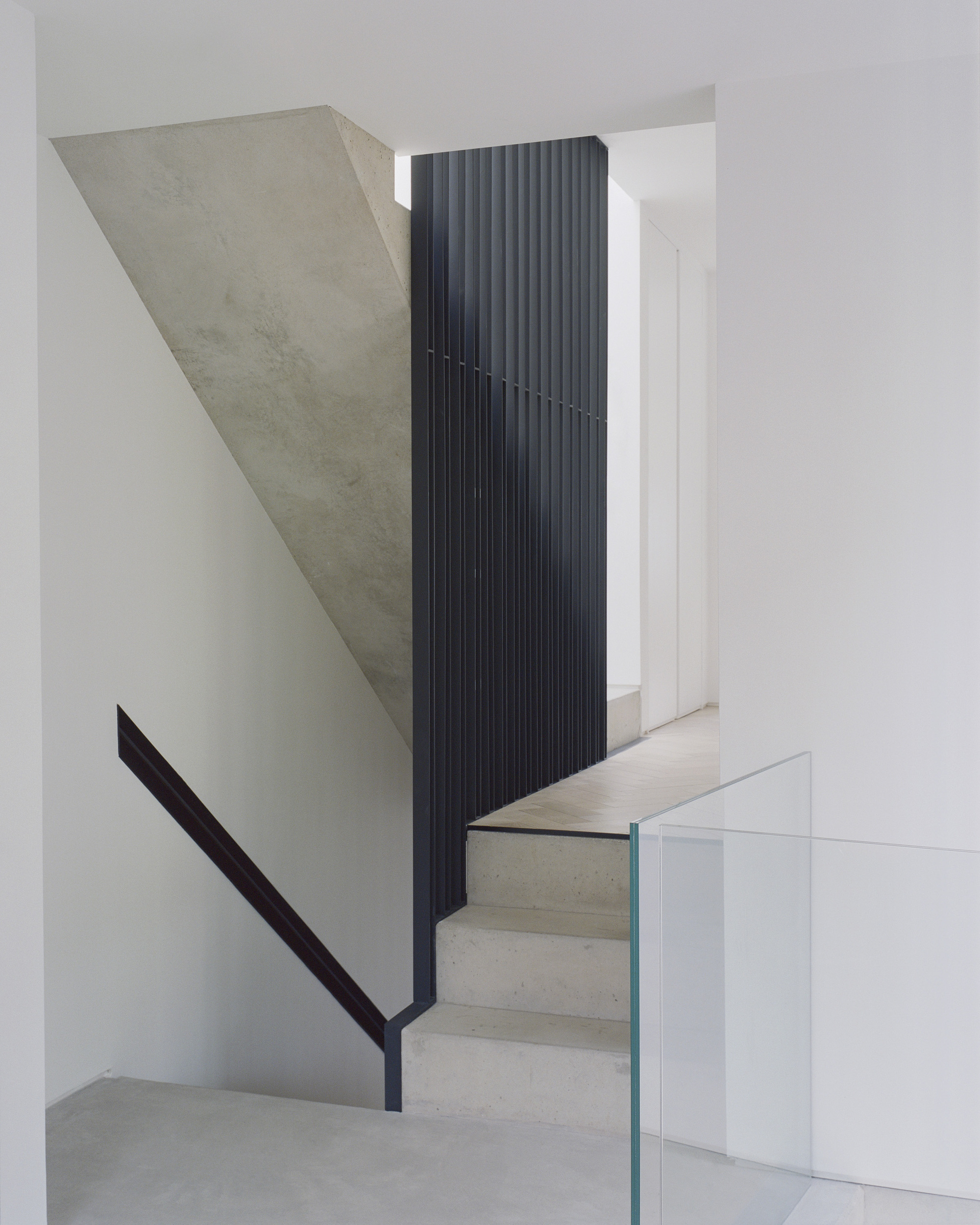 View of concrete stair landing with vertical black metal balustrade and glass guardrail below
