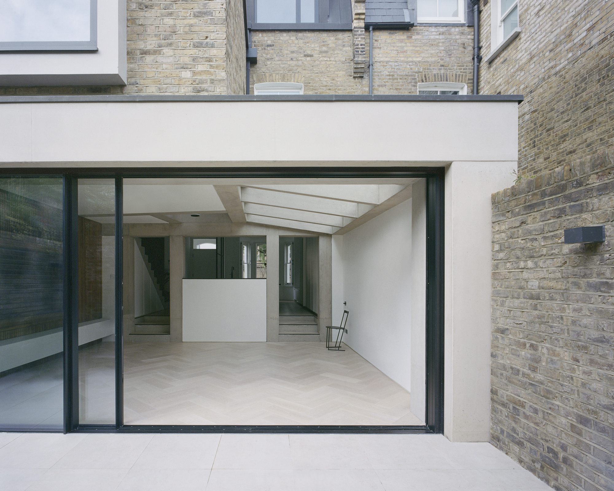 Courtyard view through sliding glass doors revealing white interior volumes beneath a linear skylight
