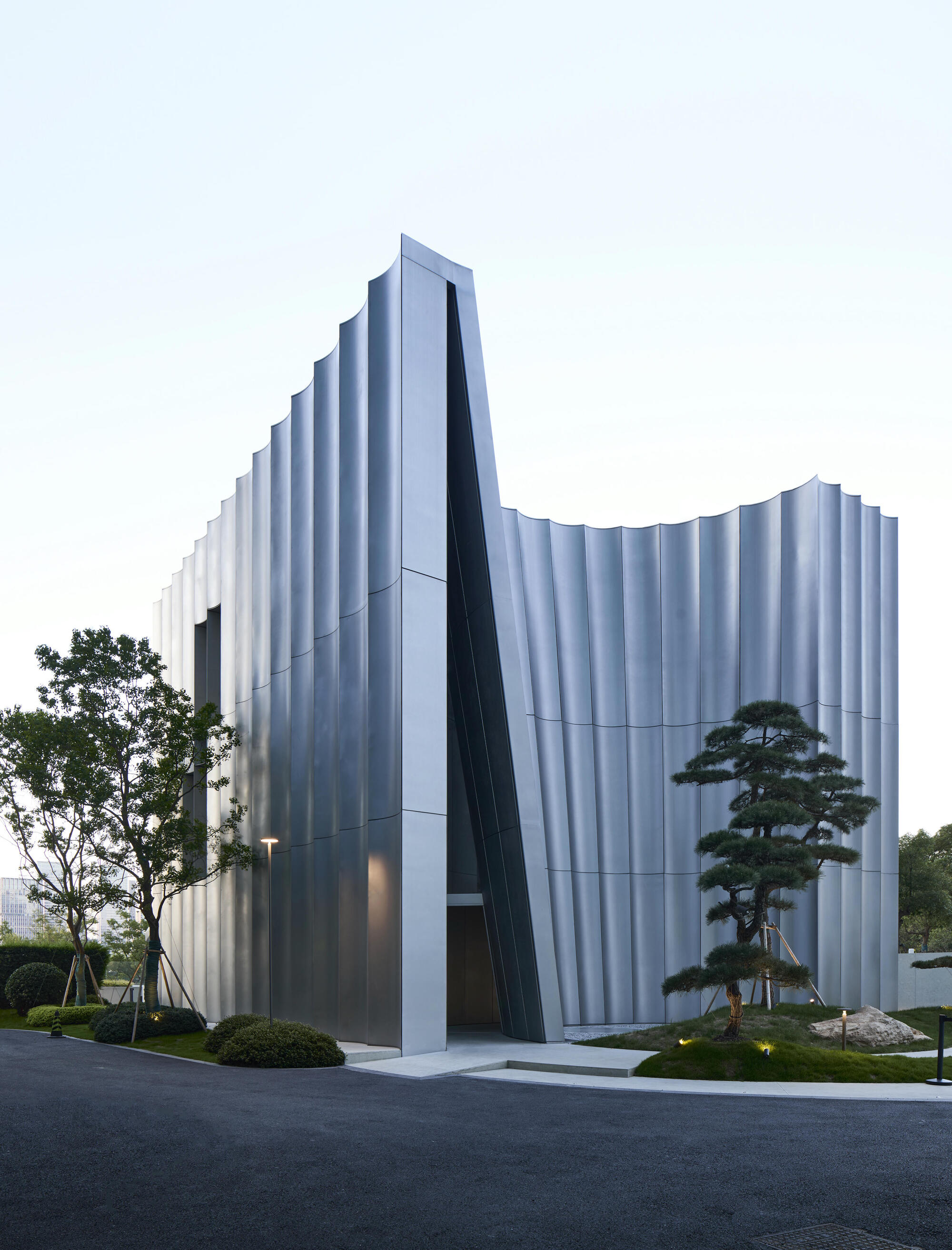 Street view of the undulating white facade with deep slanted entry void at dusk