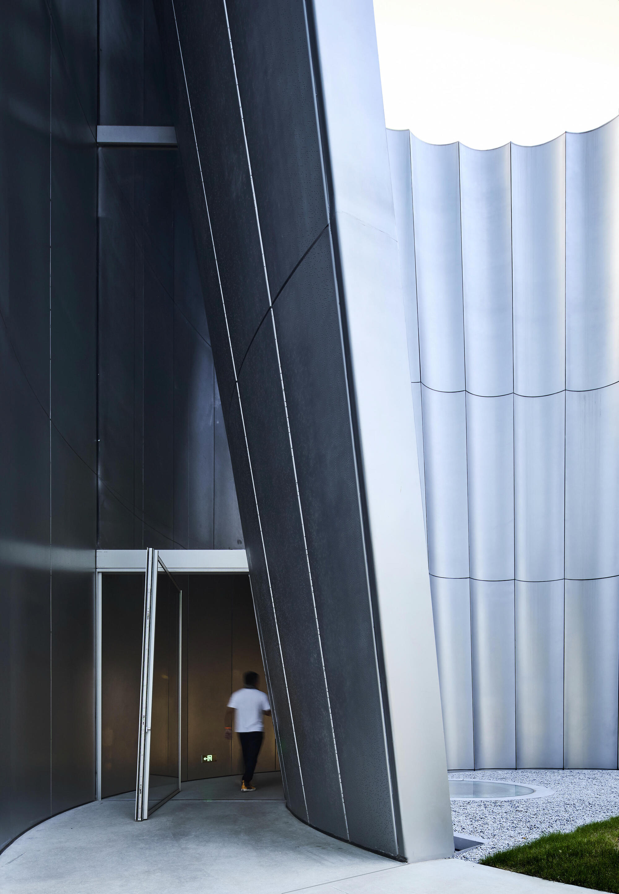 Entrance passage with dark angled wall and figure walking beneath the ribbed white exterior