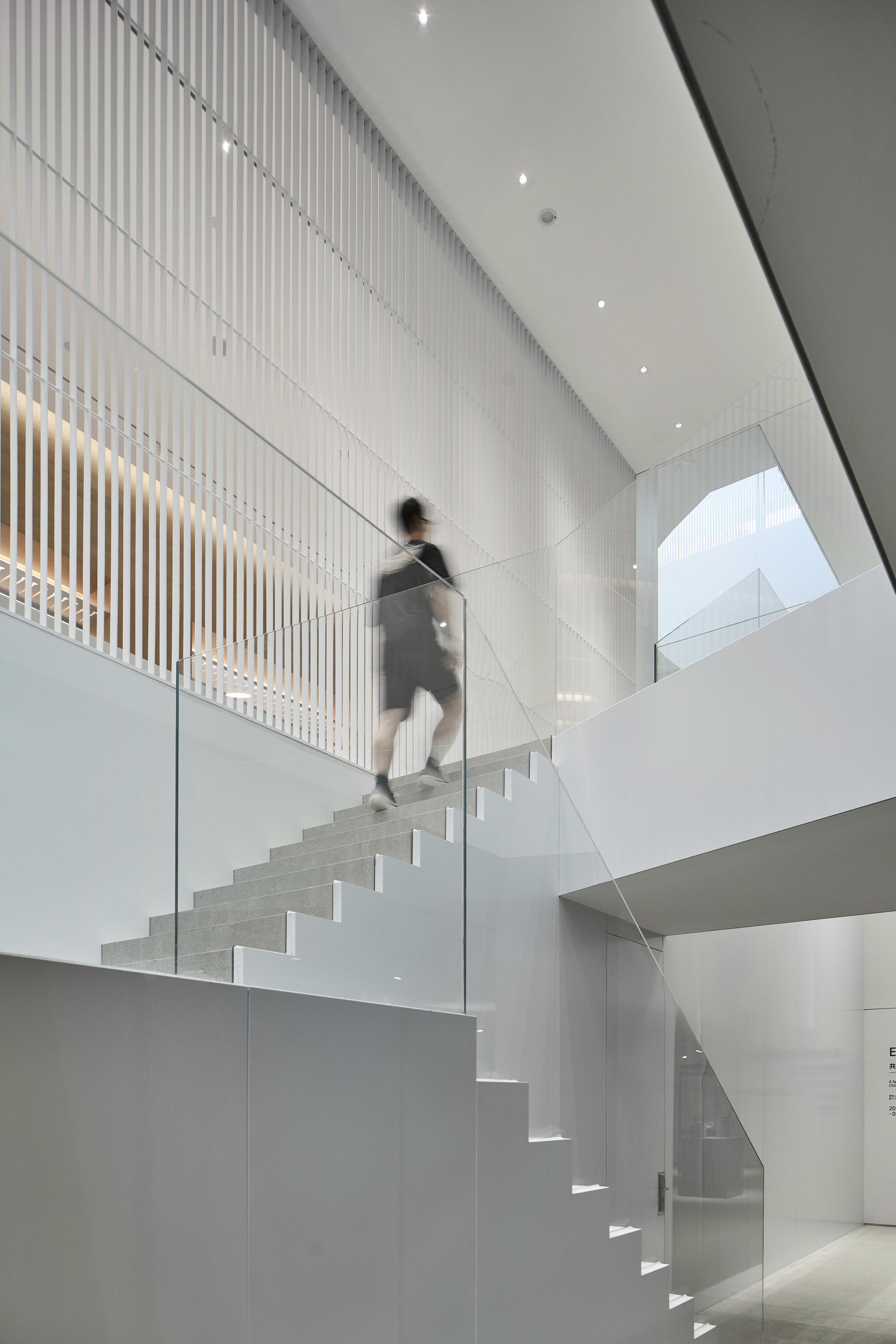 White cantilevered staircase with glass balustrade and vertical screen wall as figure descends