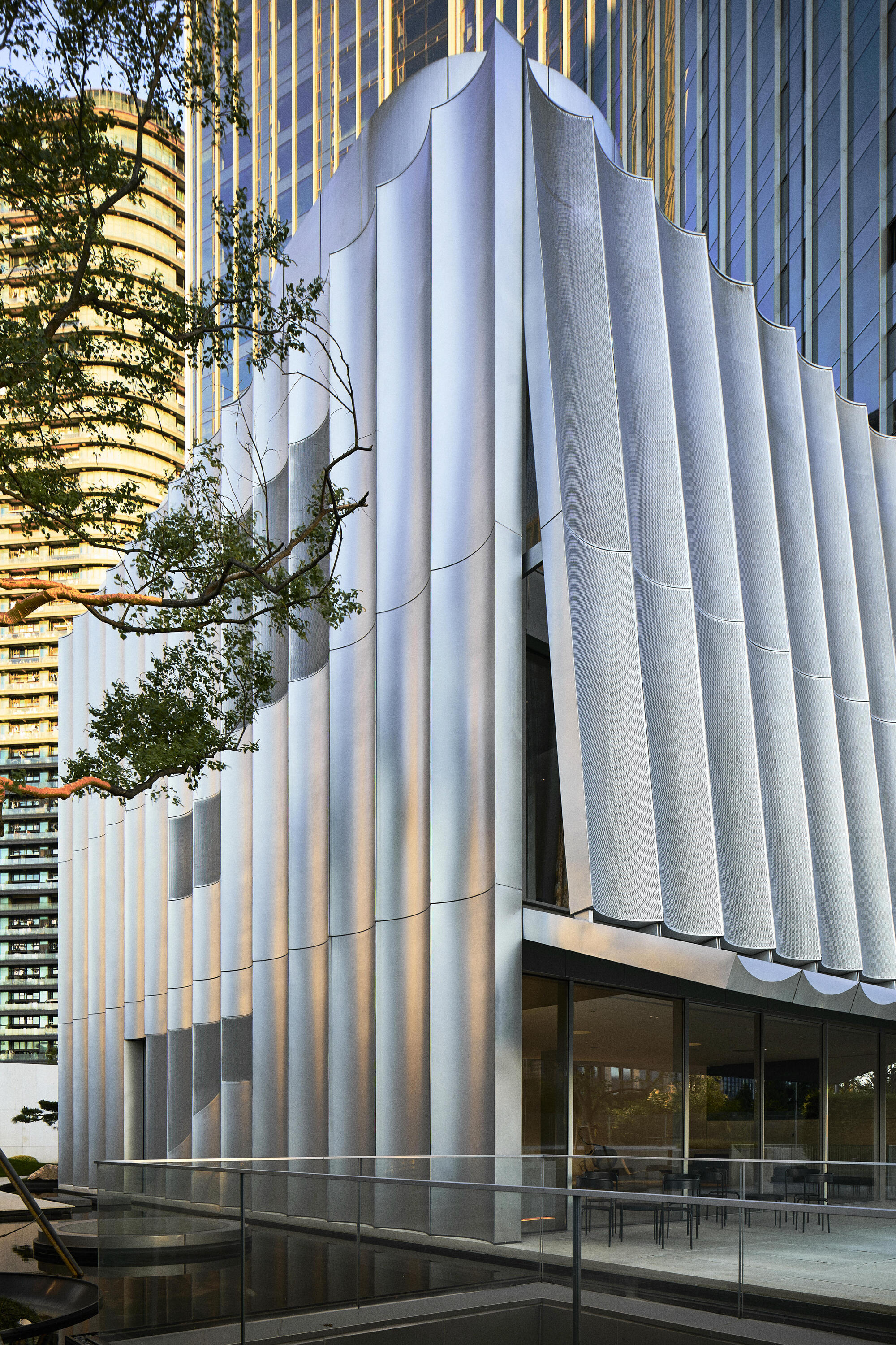 White vertical fins wrapping the facade corner with a tree branch emerging between the columns
