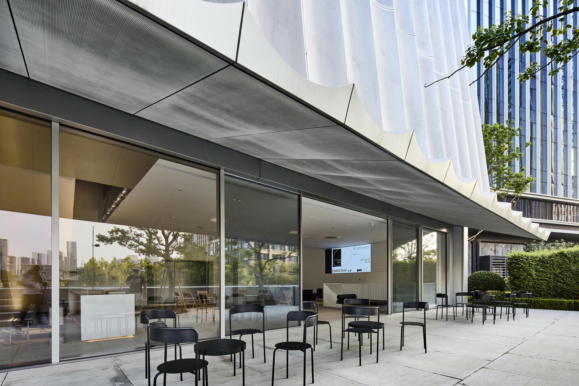Covered outdoor terrace with metal chairs beneath a perforated soffit and full-height glass walls