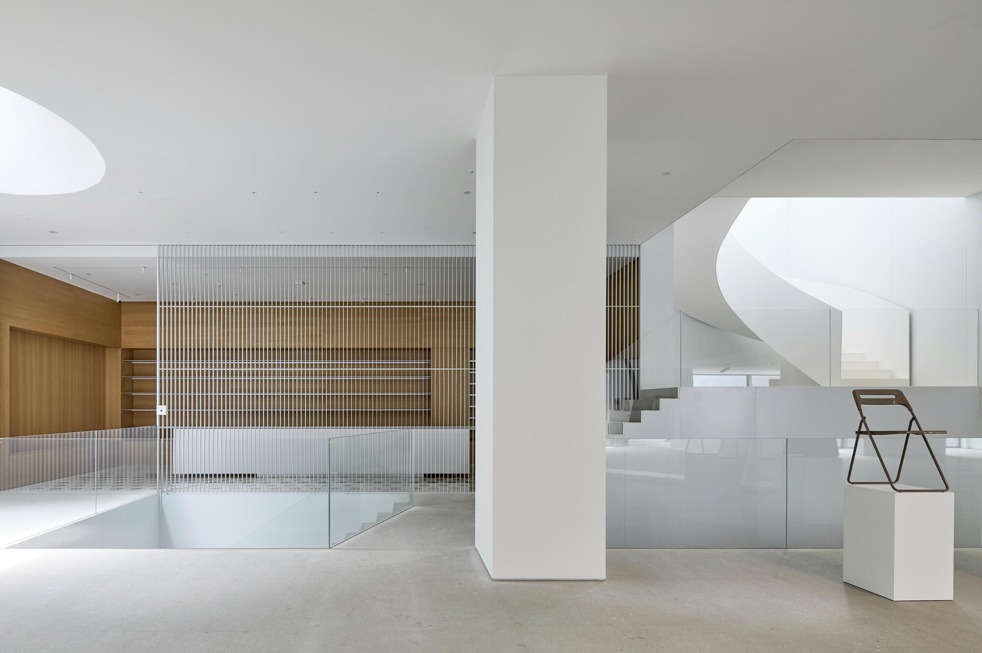 Double-height lobby space with vertical timber slat partition and curved white staircase in background