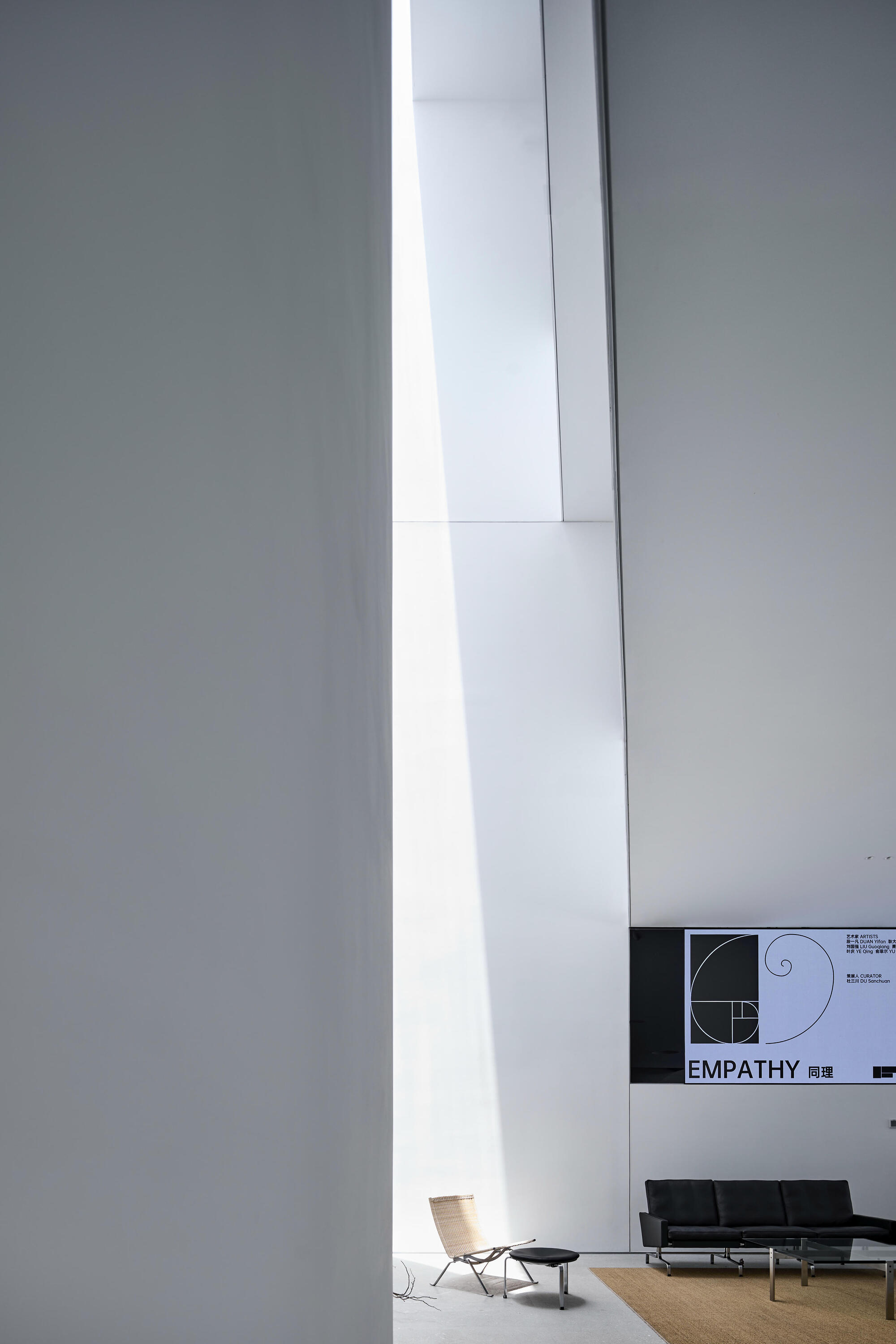 Tall vertical skylight slicing through white gallery walls with seating area visible below