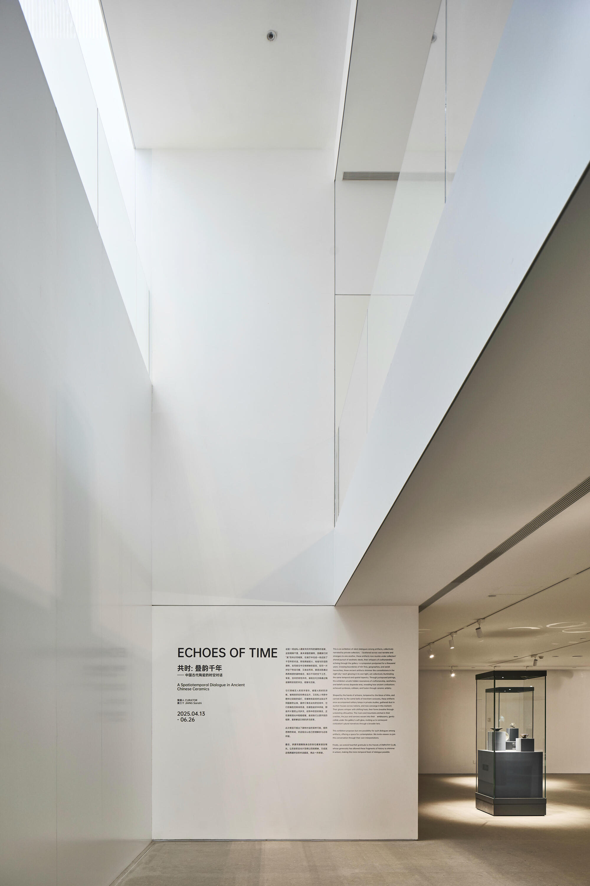 Gallery space with angular white ceiling planes, wall-mounted exhibition text, and illuminated display case