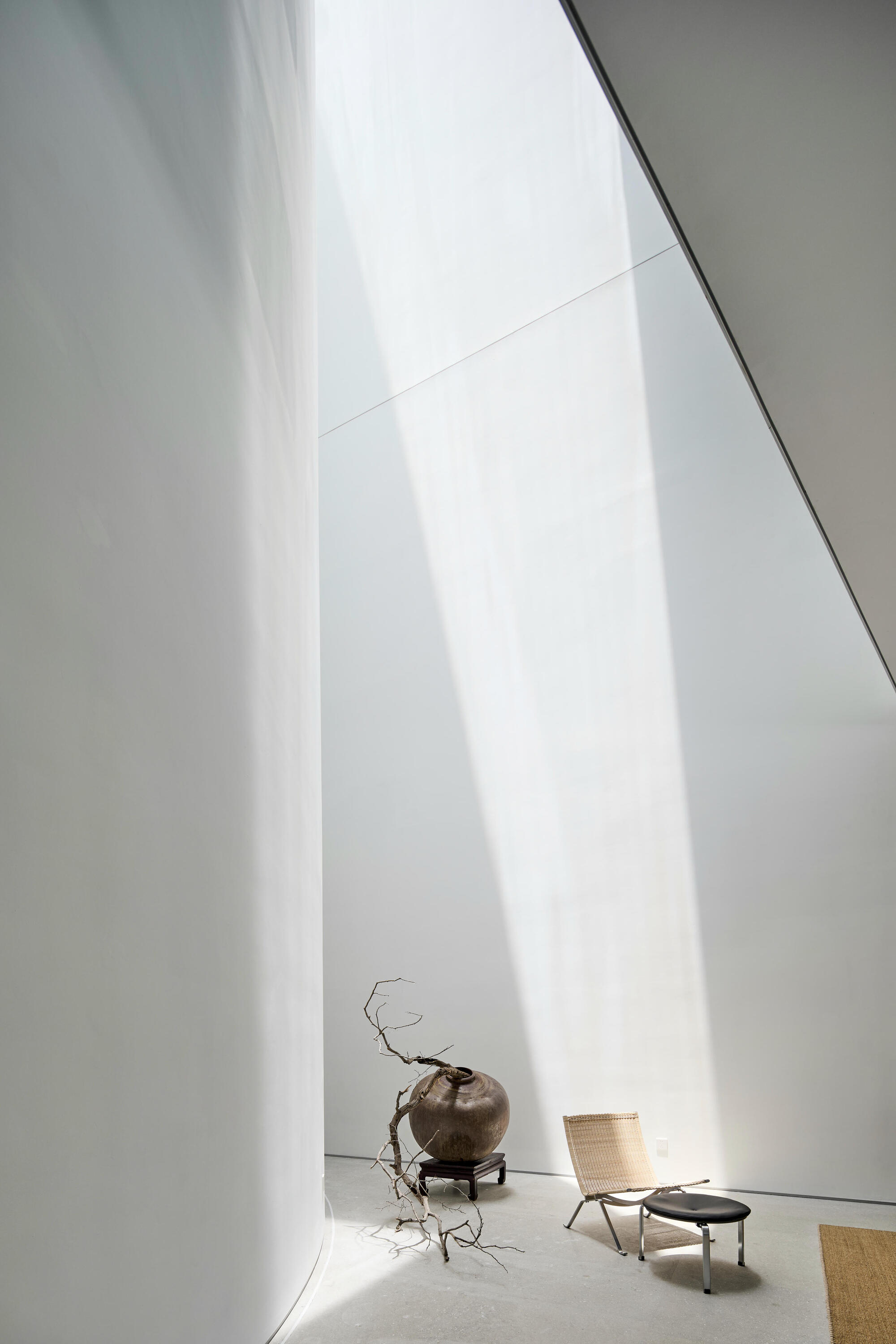 Tall gallery space with angled white walls and a sculptural branch in a vase under diffused daylight
