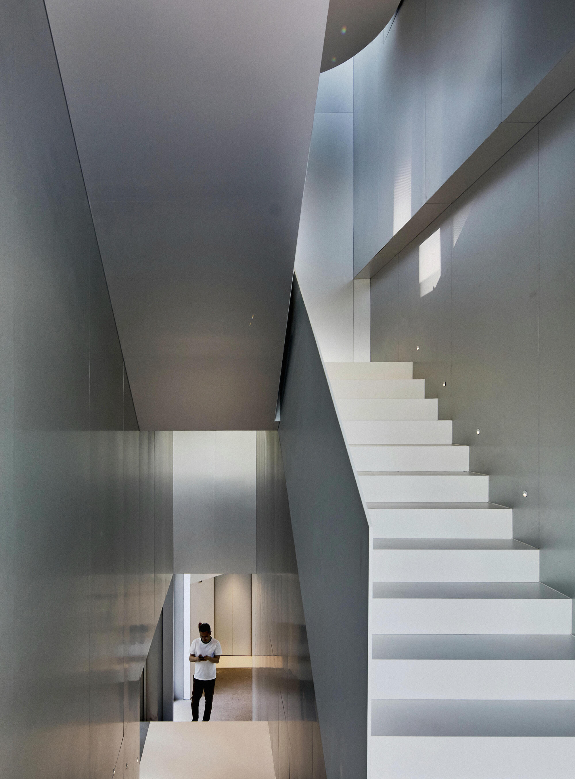 White cantilevered staircase rising through a multi-story volume with a figure visible below
