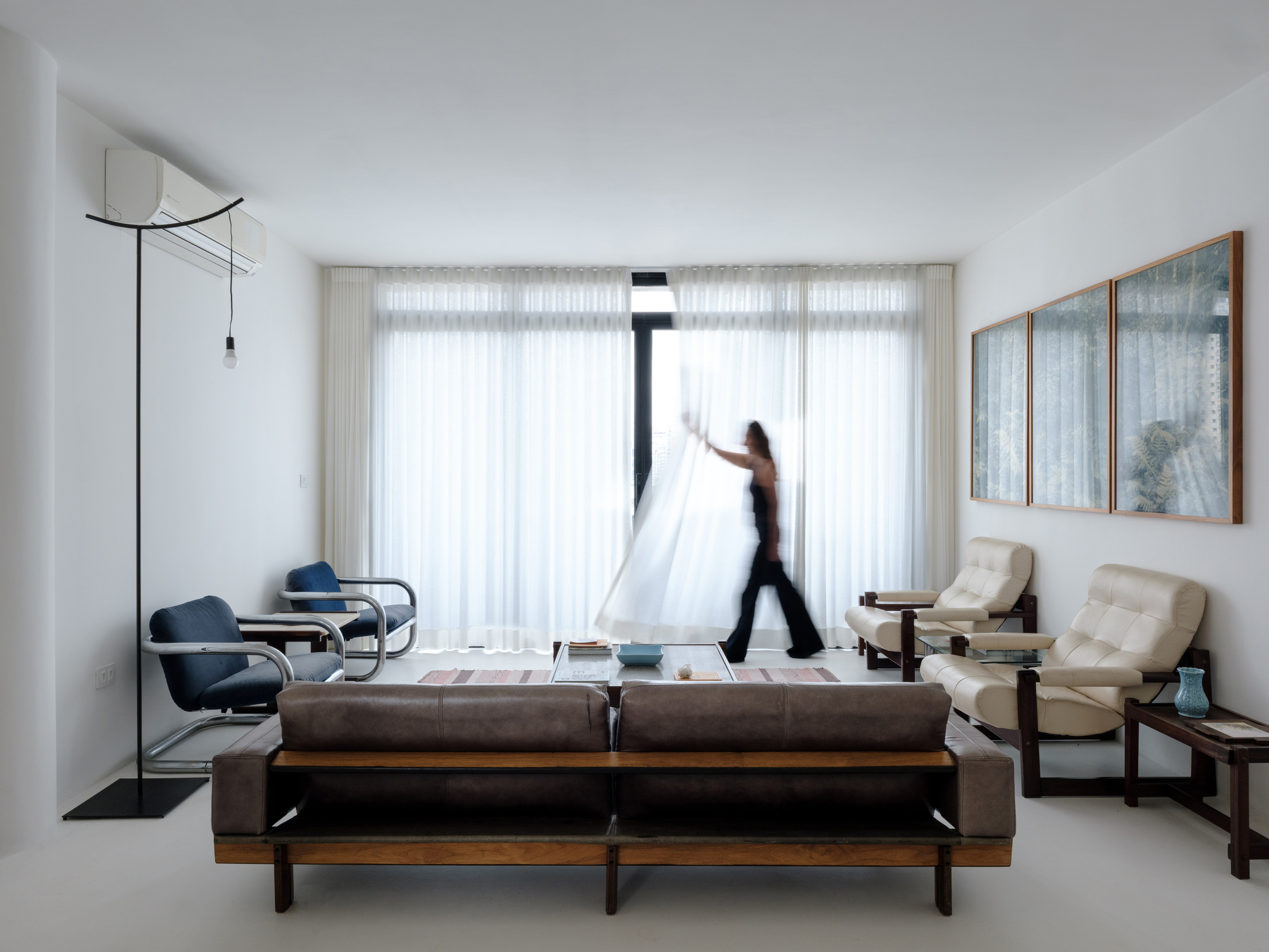 Living room with floor-to-ceiling sheer curtains and a person walking past the sofa