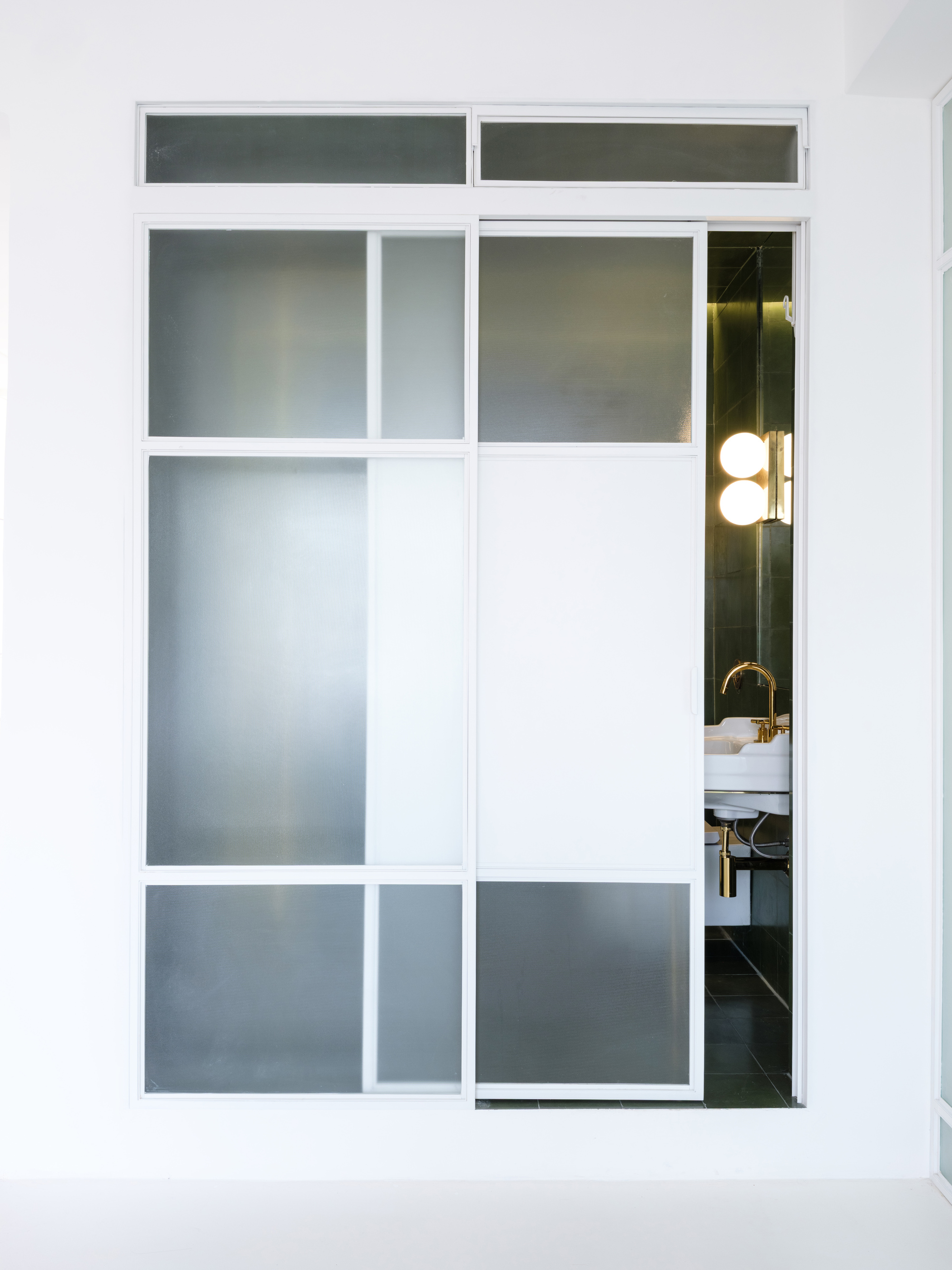 White-framed sliding door with frosted glass panels partially open to reveal a bathroom with brass fixtures