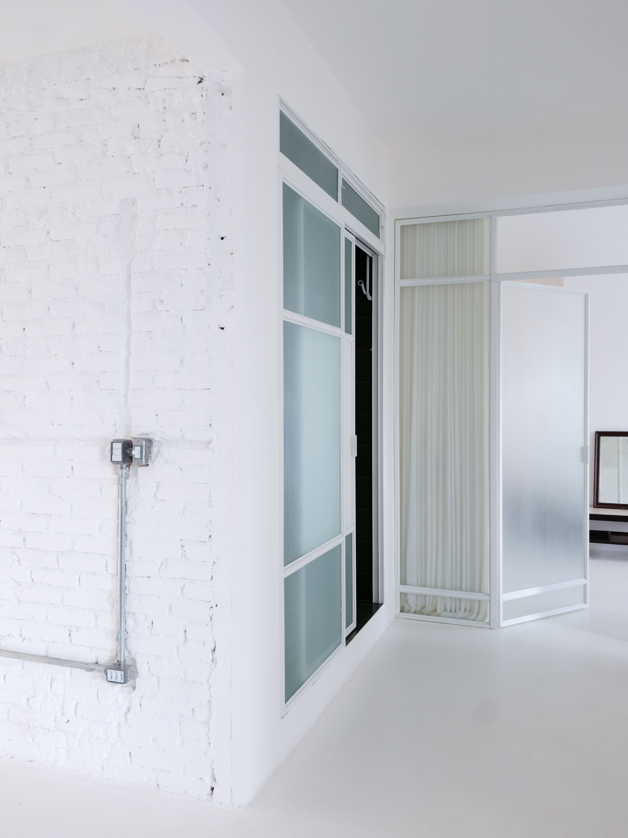 Interior partition with frosted glass panels and white frames against a painted brick wall with exposed conduit
