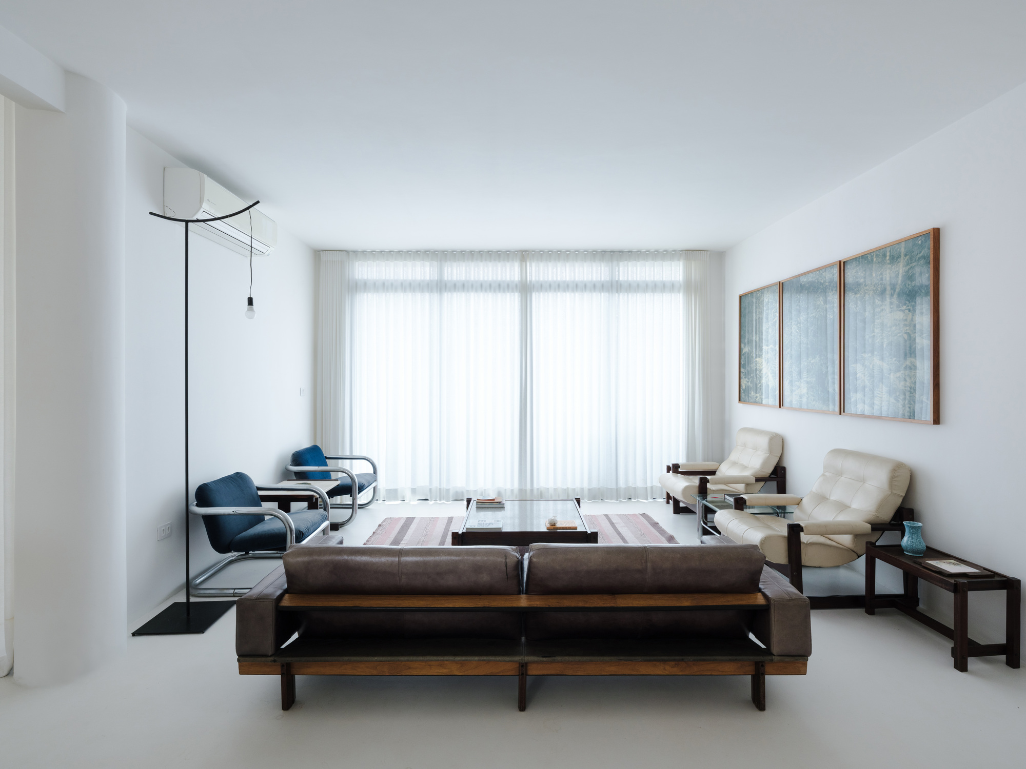 Living room with white sheer curtains spanning curved window wall and mid-century furniture on pale resin floor