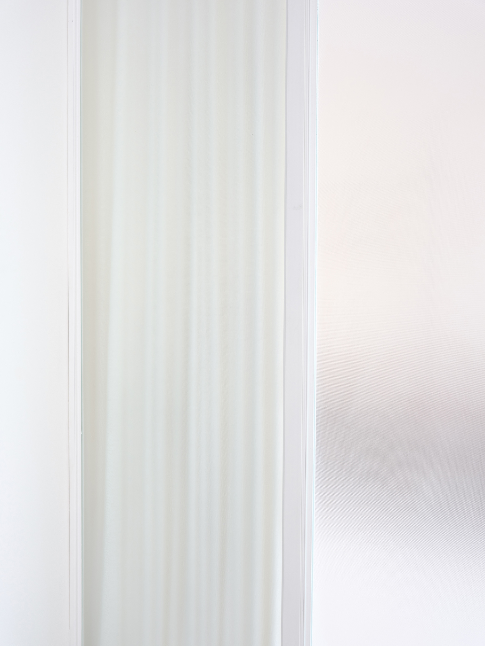 Close-up of translucent reeded glass panel framed in white metal alongside sheer curtain in soft daylight