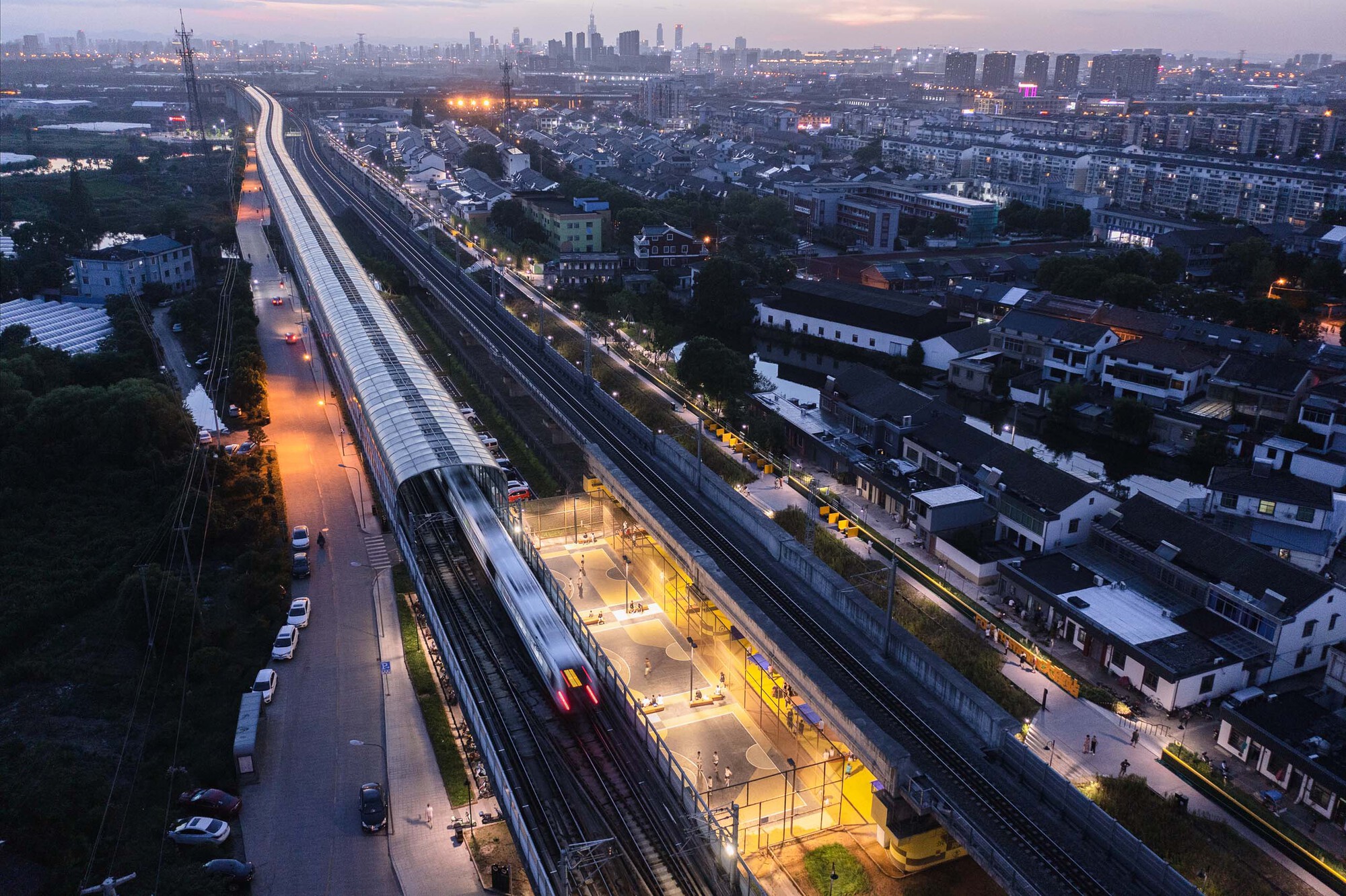 Aerial perspective of the illuminated platform canopy and yellow play areas along the tracks at dusk