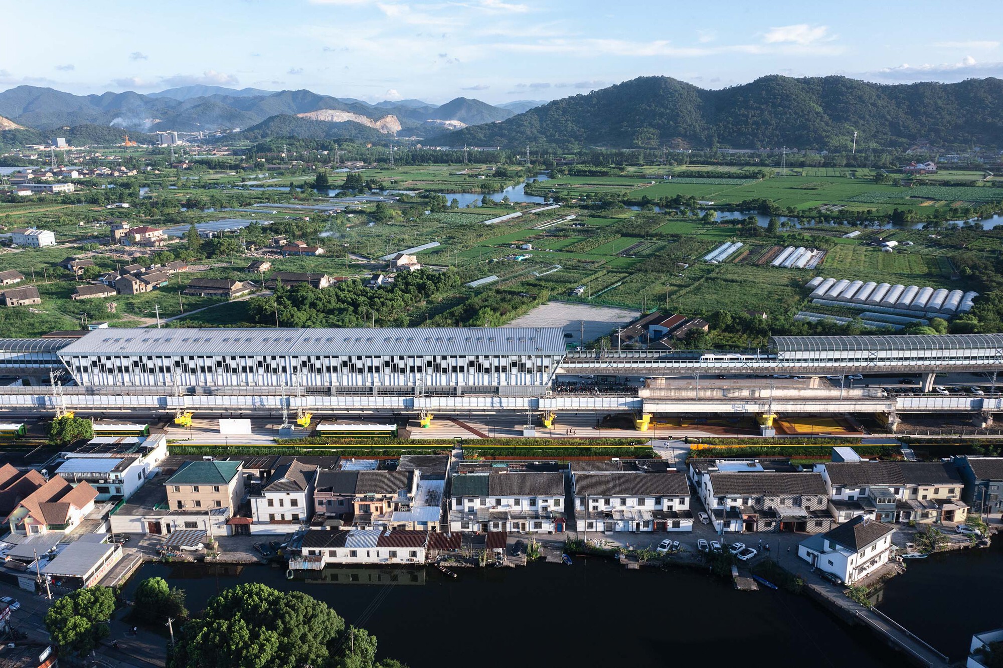 Aerial view of elevated station with tubular skylights spanning parallel rail tracks across agricultural landscape