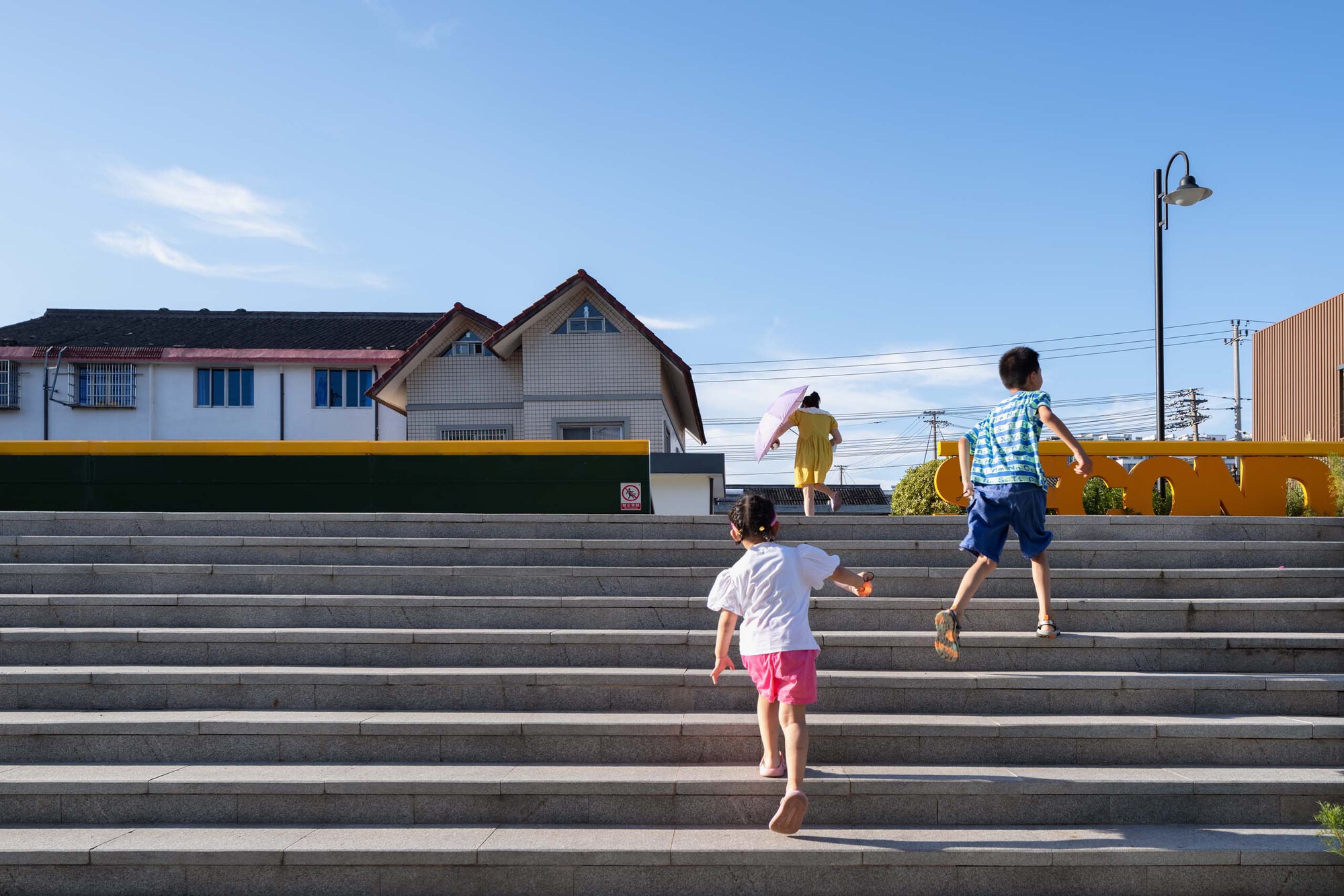 Wide concrete steps with children running up them beneath a blue sky and streetlamp