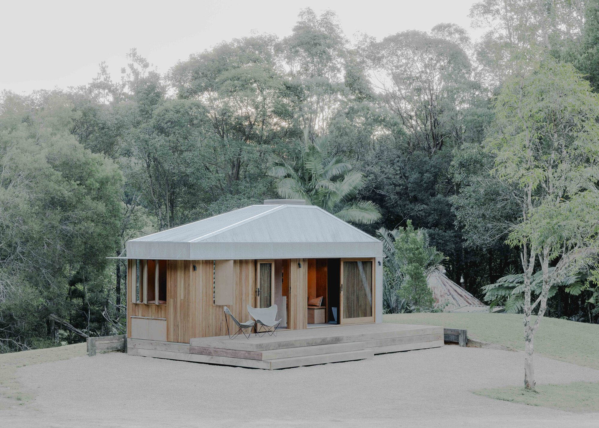 Timber-clad pavilion with corrugated metal roof and timber deck terrace surrounded by dense tree canopy