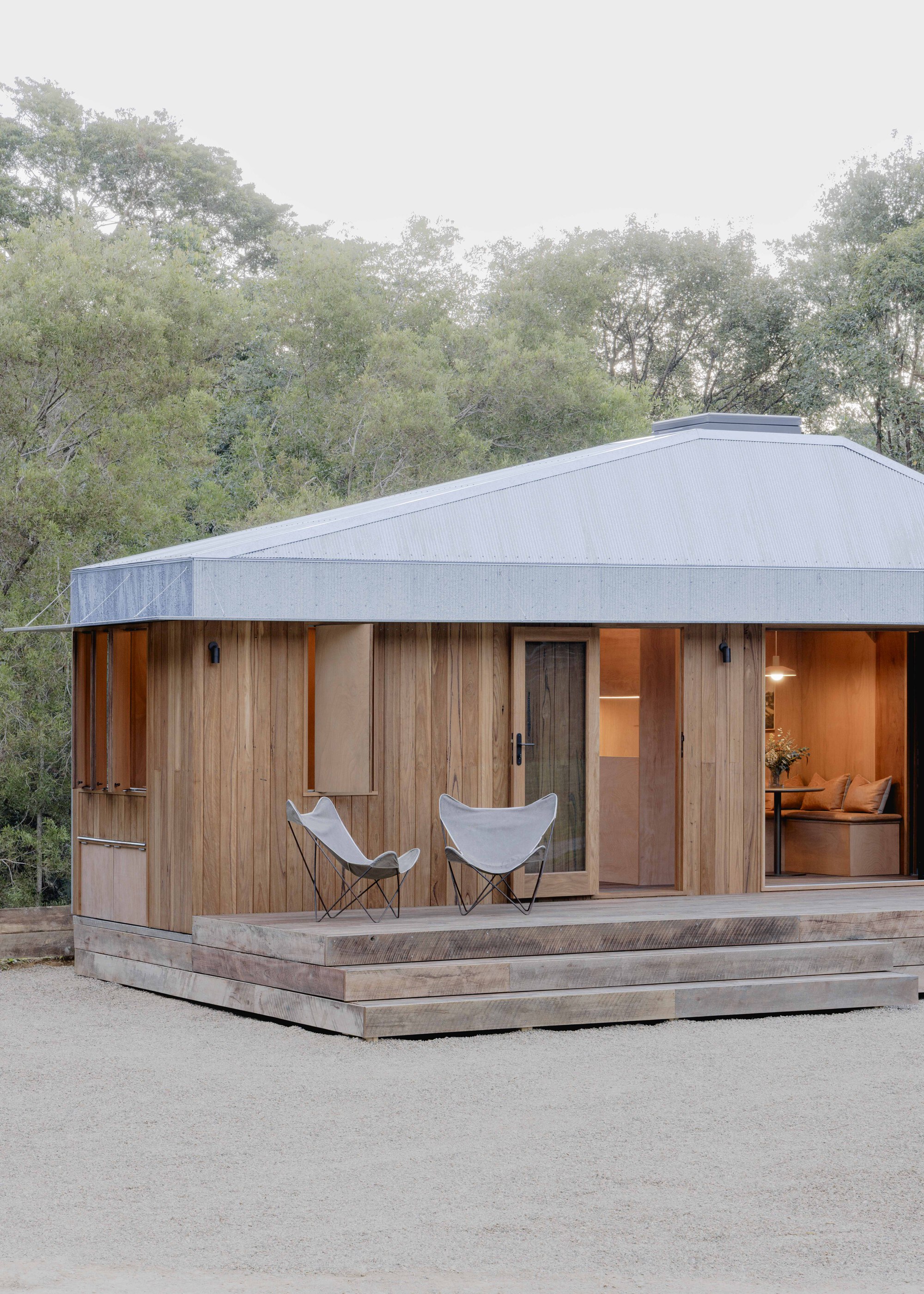 Front elevation showing vertical timber cladding with glazed openings and two canvas chairs on the deck