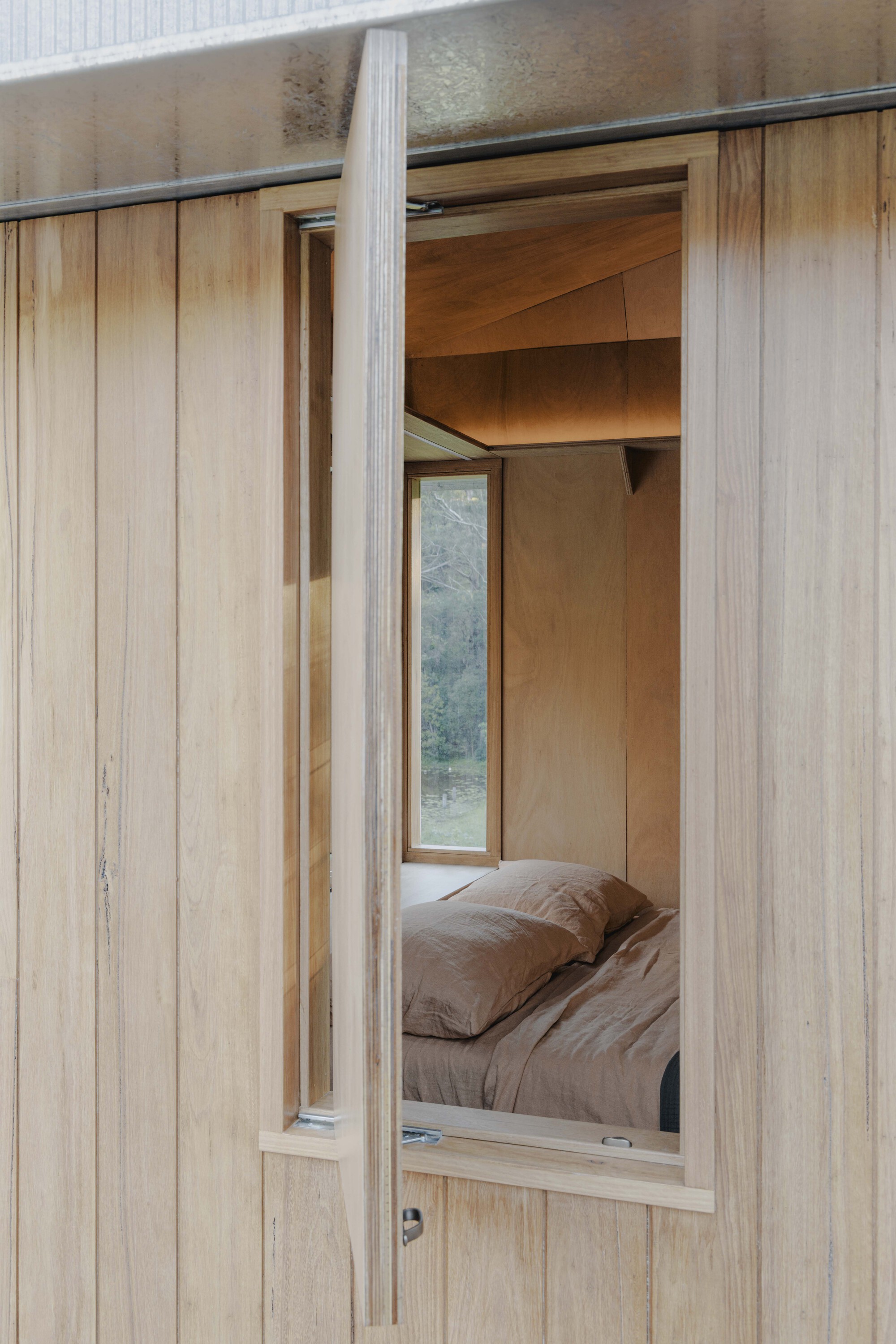 Vertical timber cladding frames the open doorway revealing the plywood-lined bedroom within