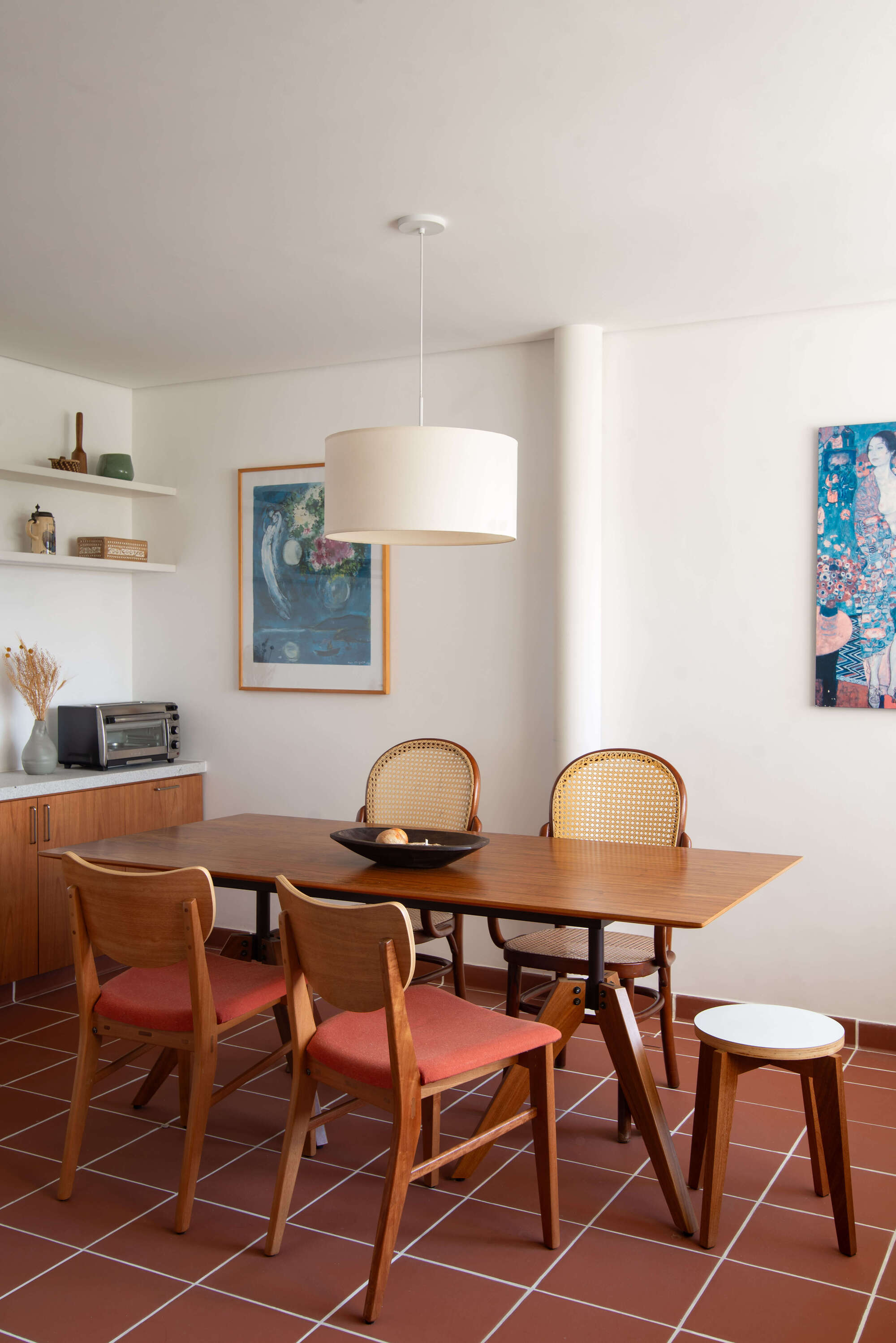 Dining area with wooden table and cane-backed chairs on terracotta tile floor under pendant light