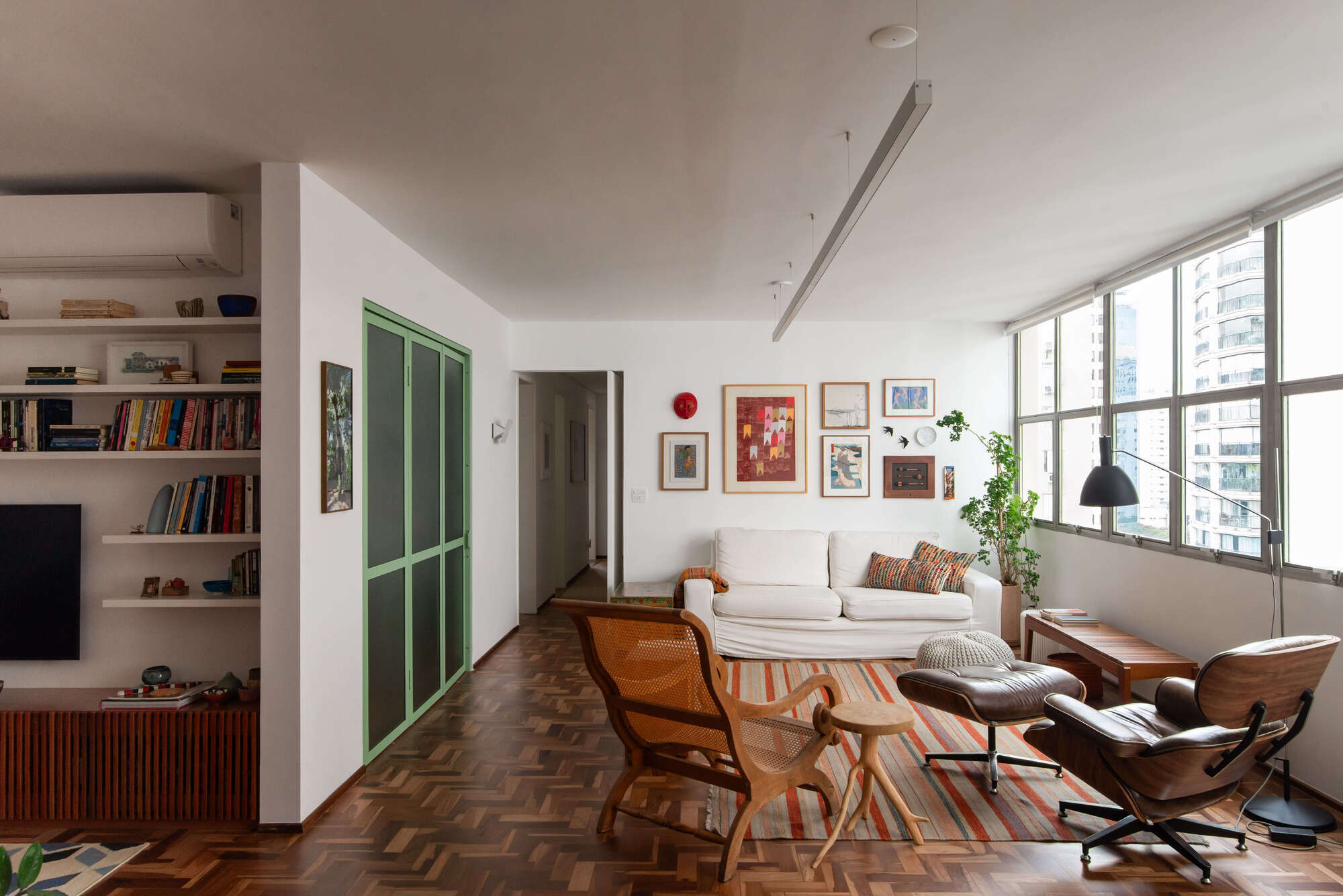 Living room with herringbone wood floor, green-framed sliding doors and floor-to-ceiling windows overlooking the cityscape